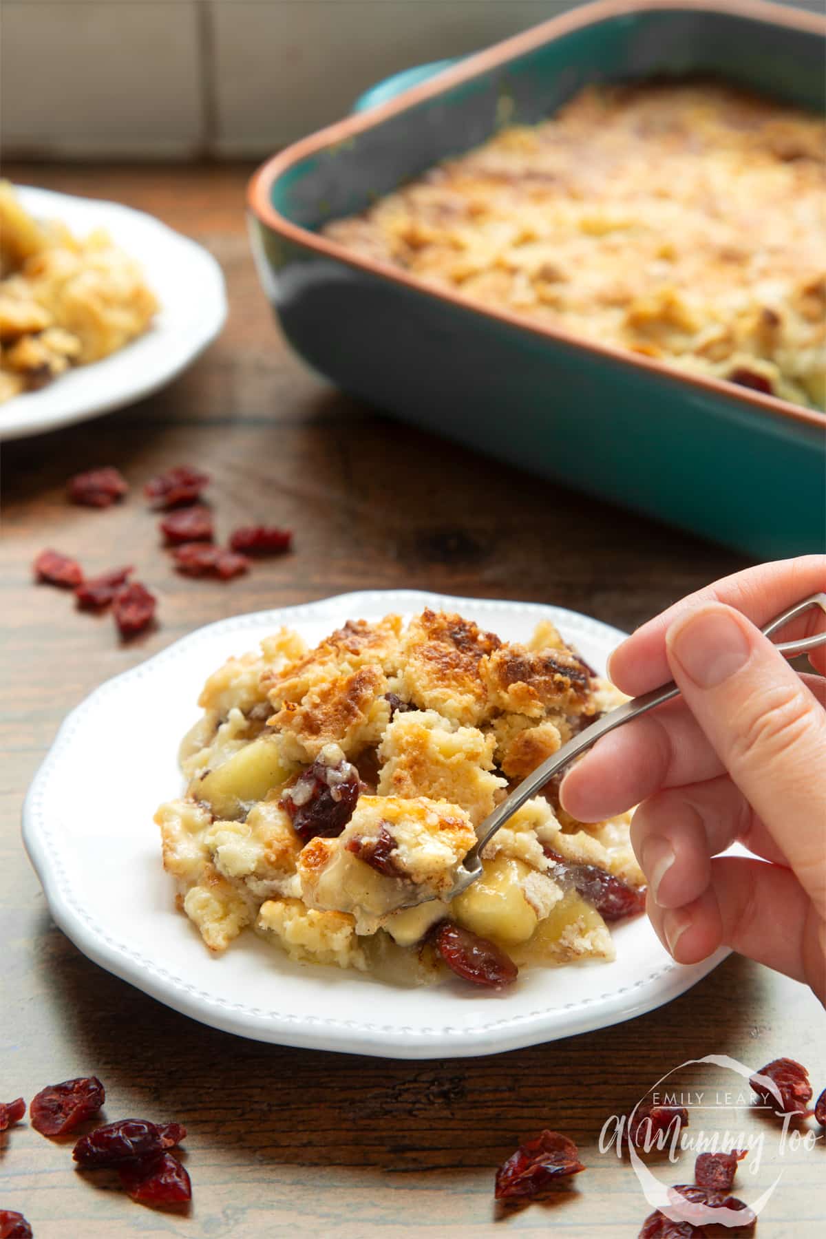 Apple cranberry dump cake served onto a small white plate. A hand holds a small spoon, which is delving into the cake.