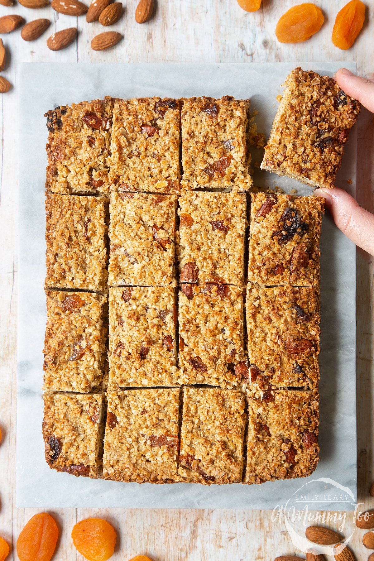 Overhead shot of a hand picking up a Apricot oat slice from a lined baking tray