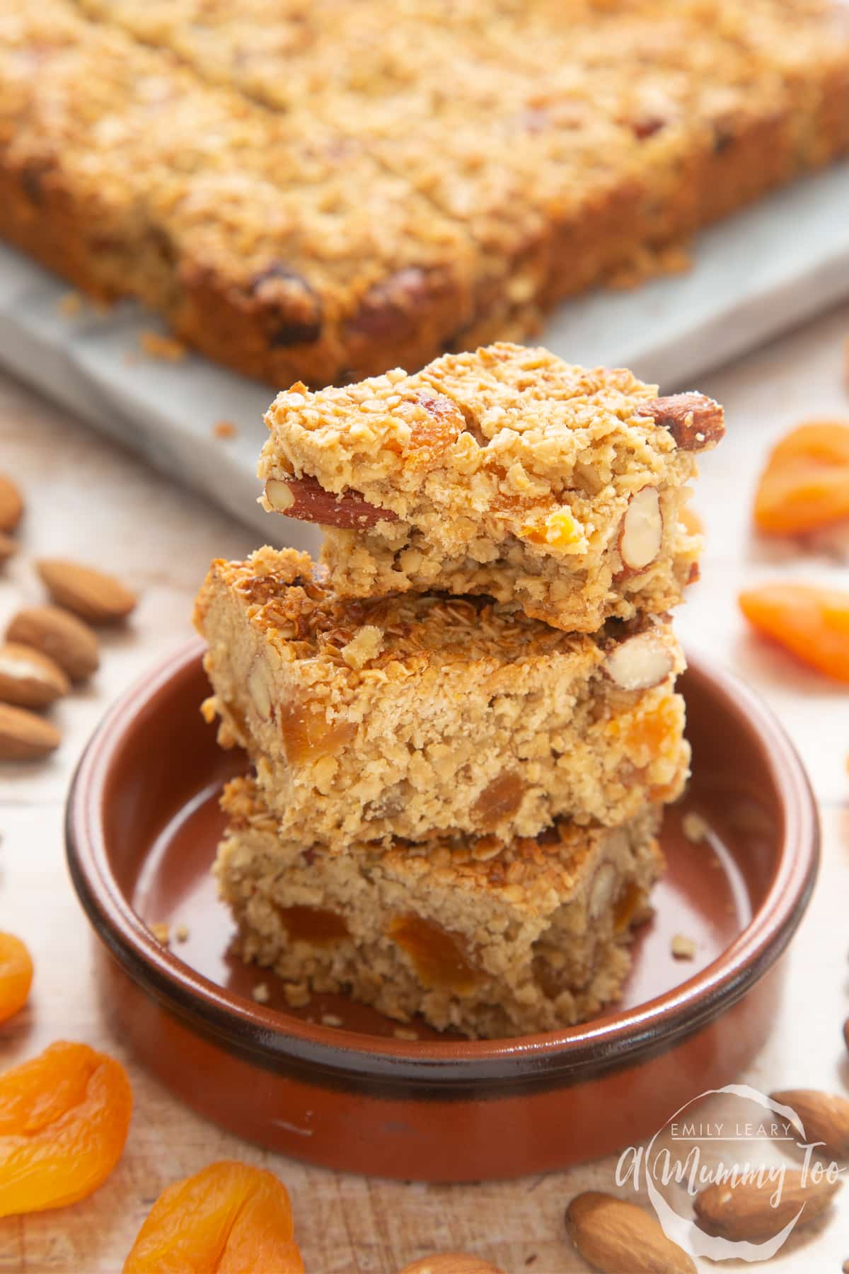 Front view shot of Apricot oat slices stacked in a brown bowl with a bite missing from the top one