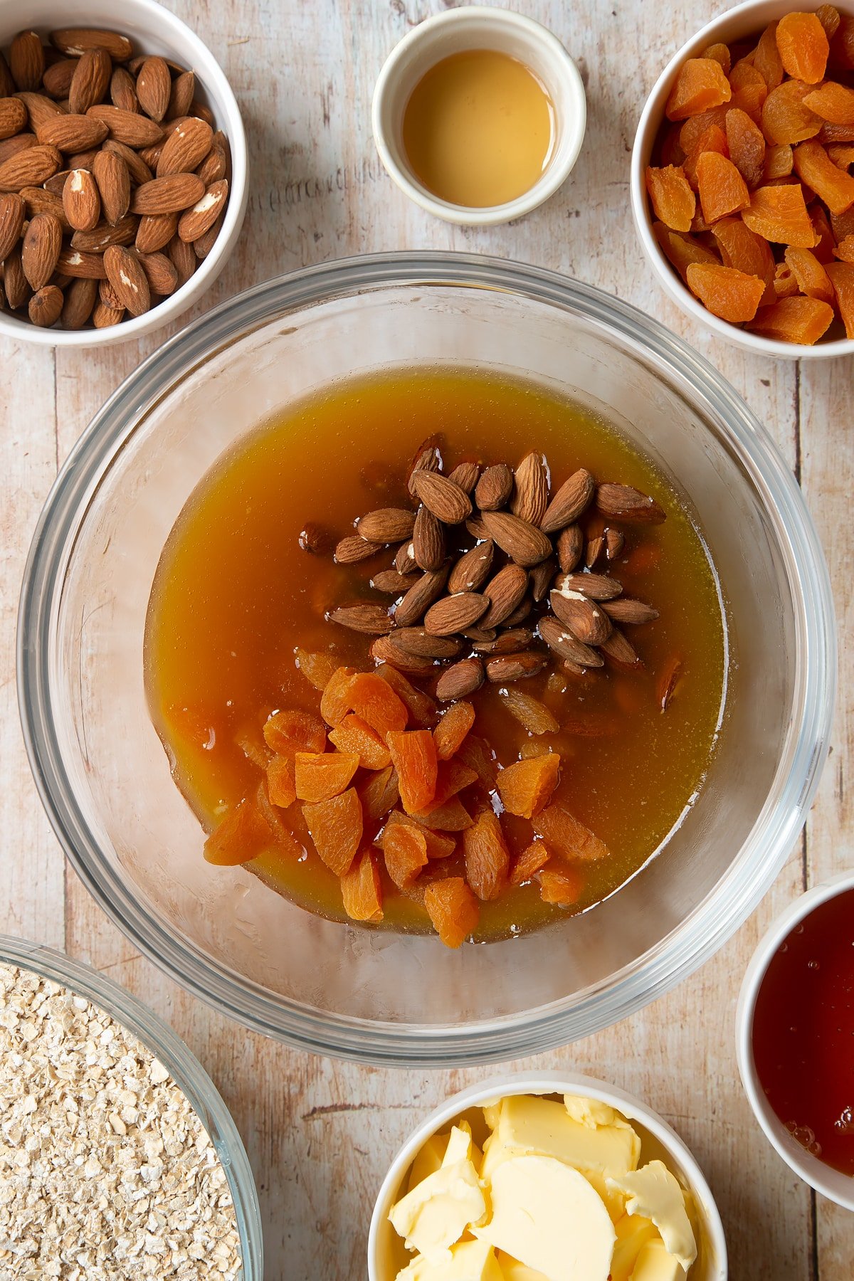 Overhead shot of liquid mixture, apricots and nuts in a large clear bowl