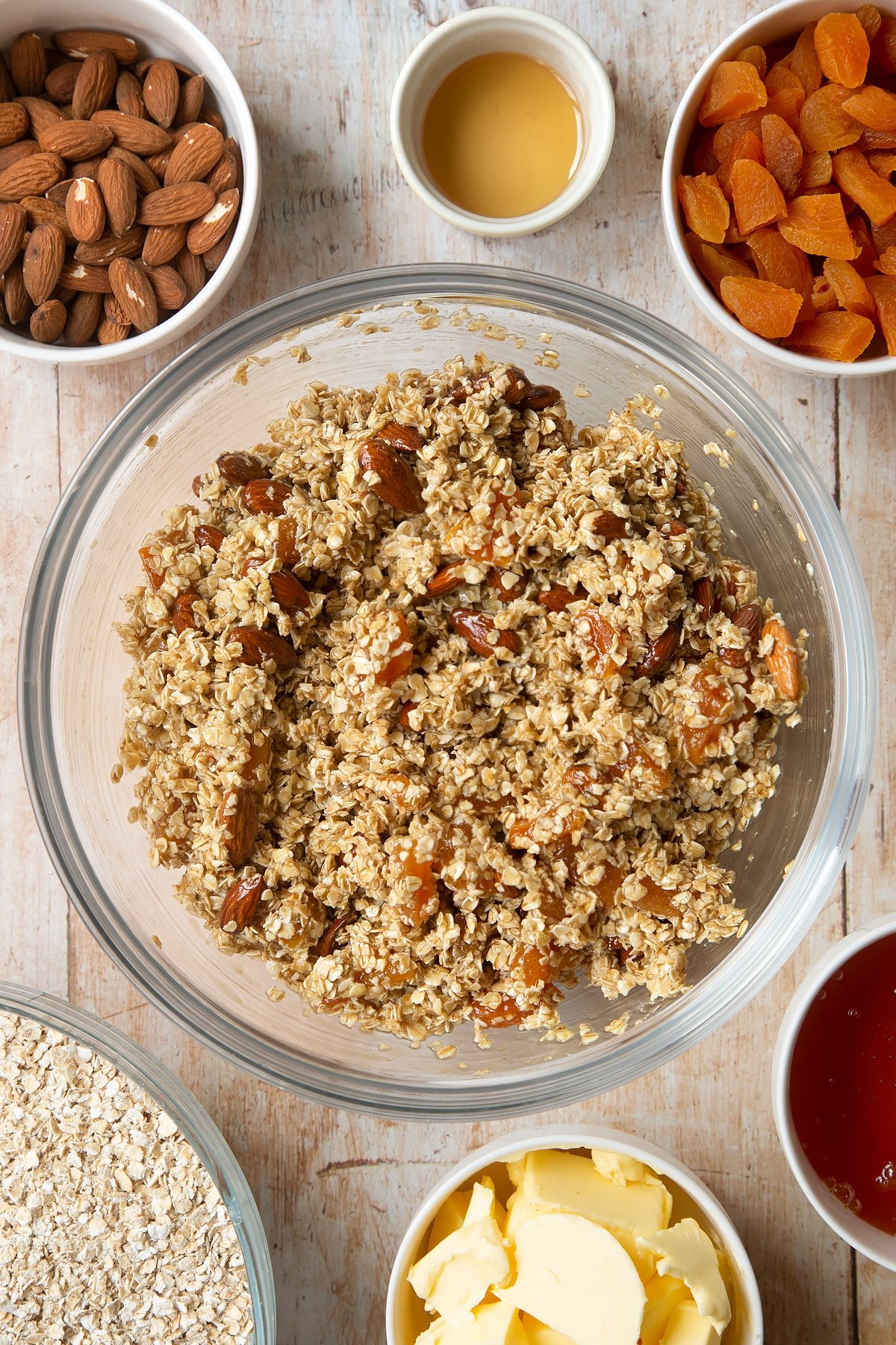 Overhead shot of oats, liquid mixture, apricots and nuts in a large clear bowl