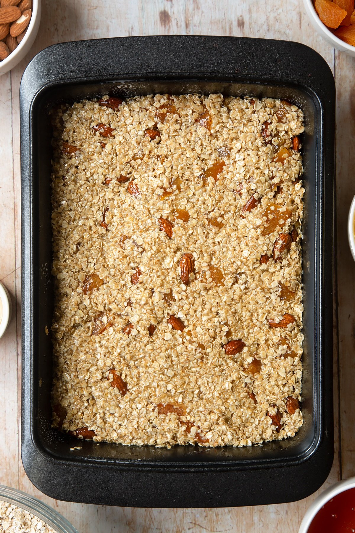 Overhead shot of flattened oat mixture in a black baking tin