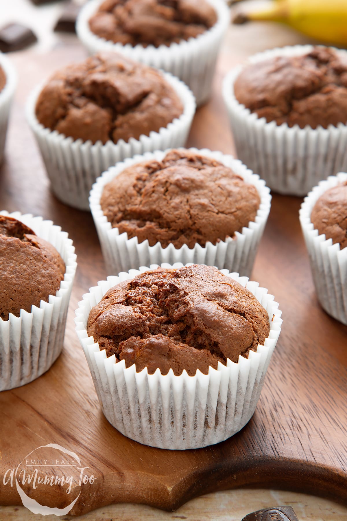 Front angle shot of Banana and chocolate muffins served on a wooden plate with a mummy too logo in the lower-left corner