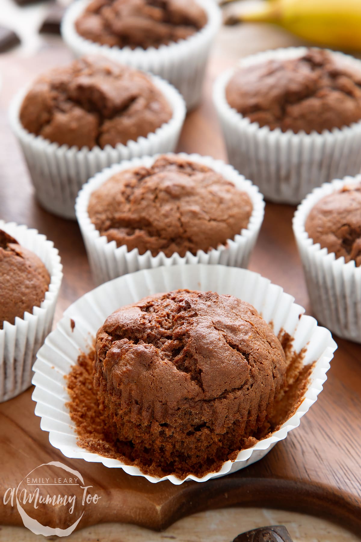 Front angle shot of banana and chocolate muffins with opened muffin cases served in a wooden plate