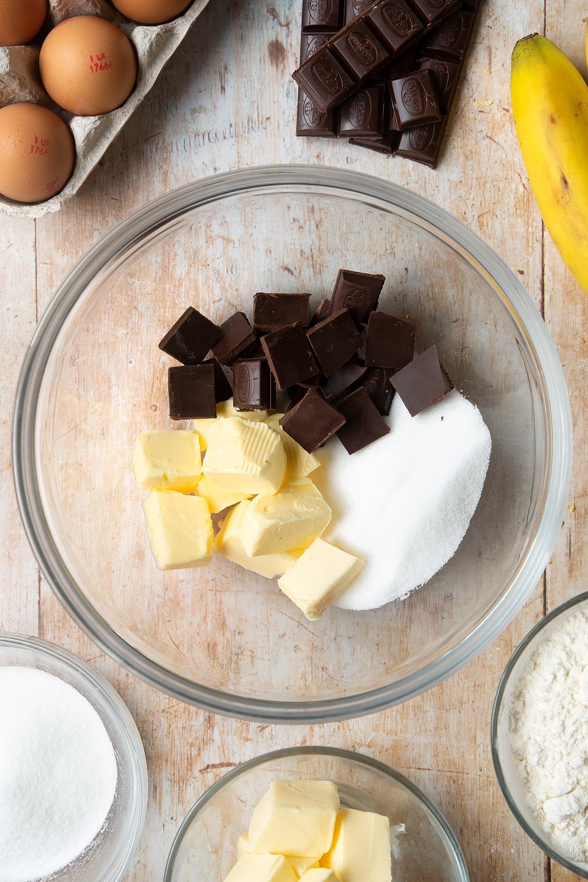 Overhead shot of butter, sugar, and chocolate in a large clear bowl