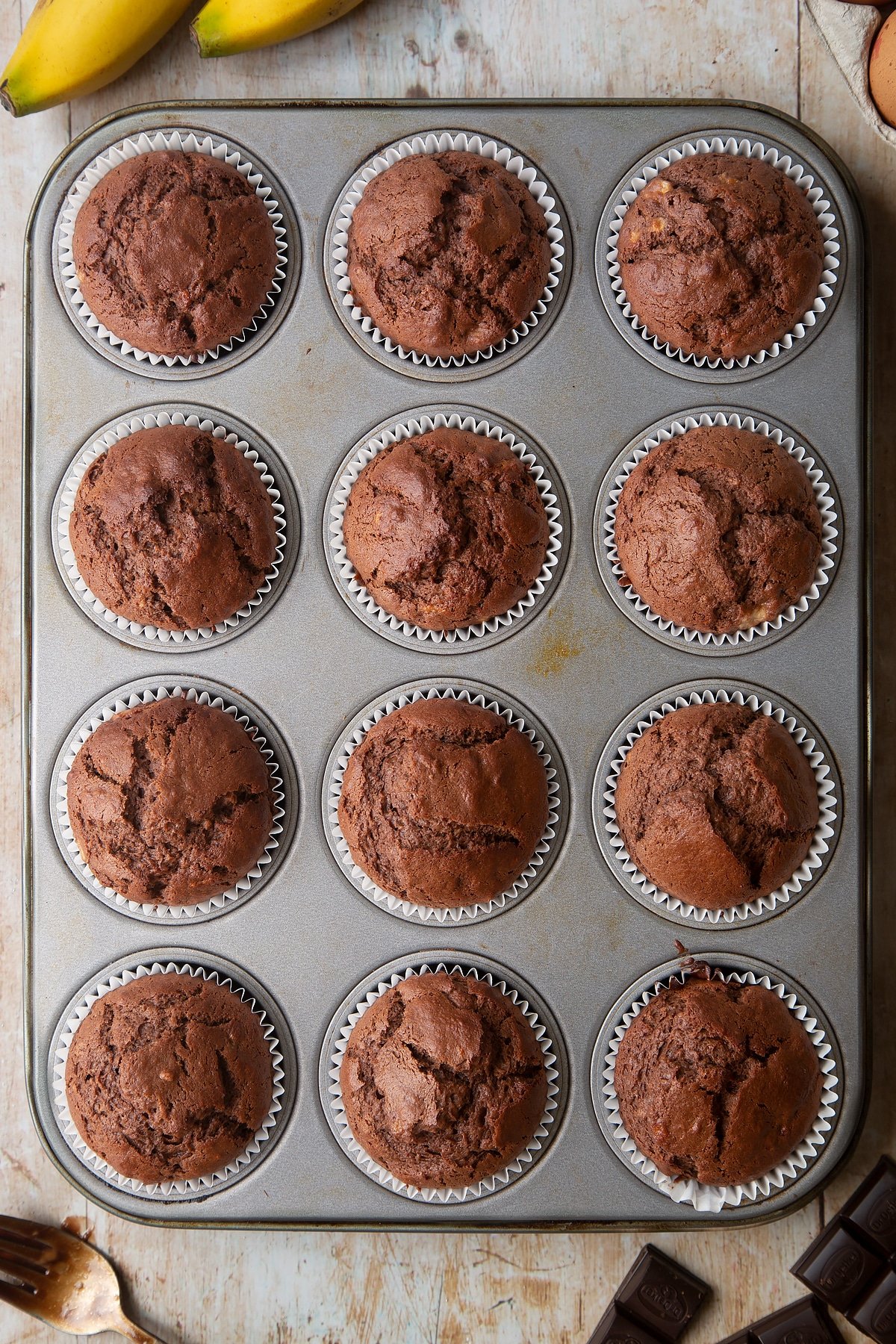 Overhead shot of banana and chocolate muffin mix with muffin cases in a muffin tray