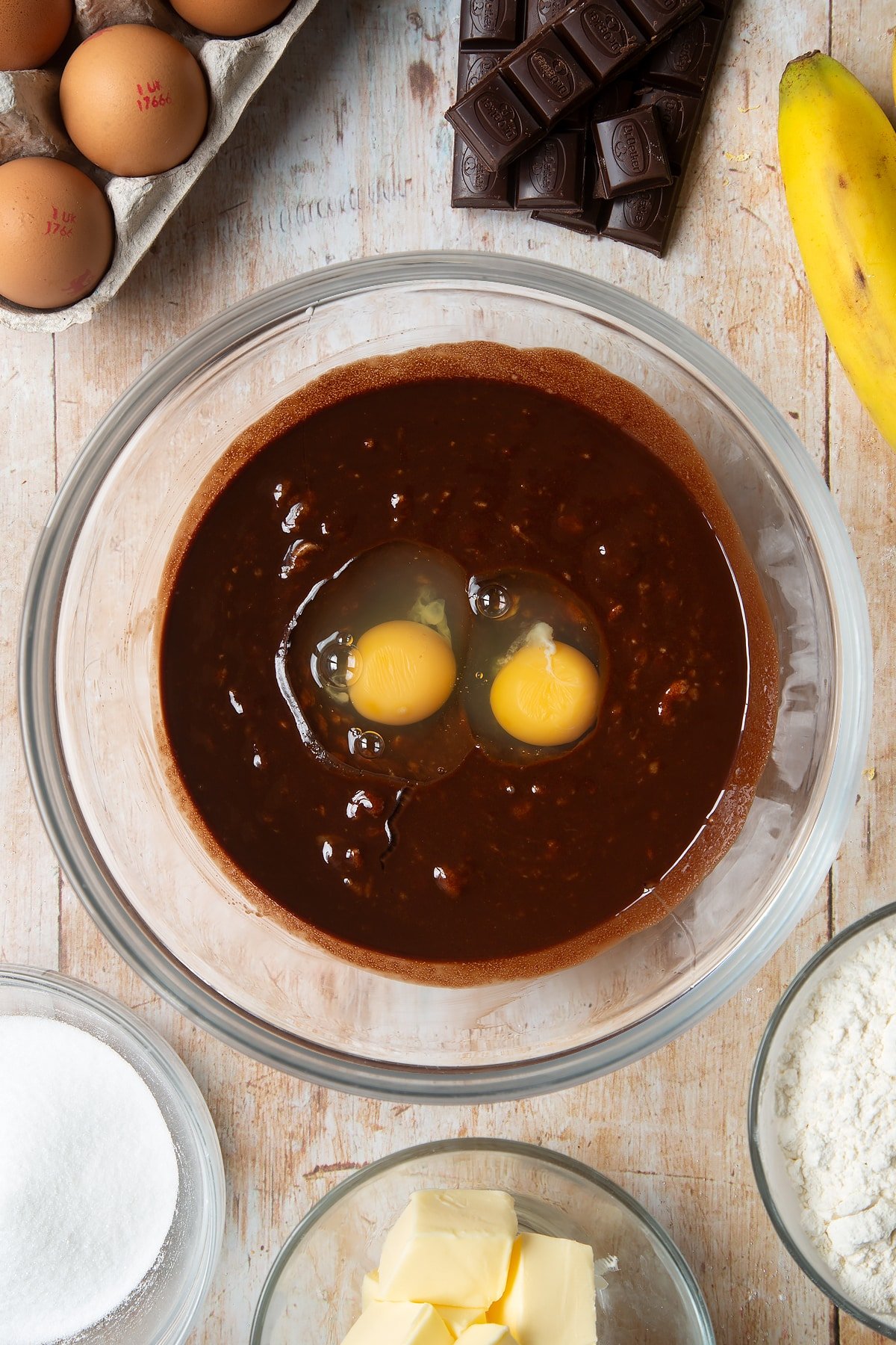 Overhead shot of chocolate liquid mixed with mashed bananas in a large clear bowl