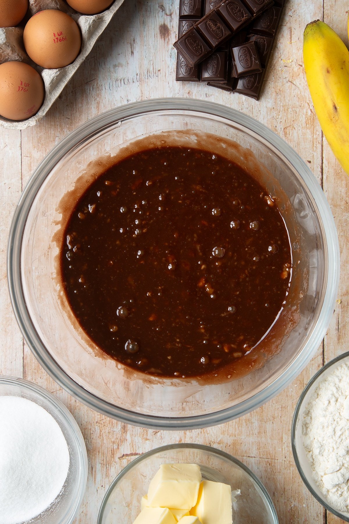 Overhead shot of chocolate liquid and two eggs in a large clear bowl