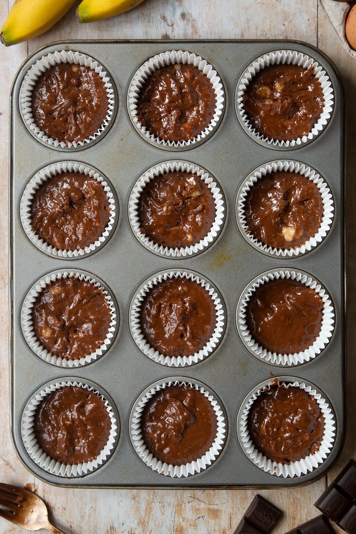 Overhead shot of banana and chocolate muffin mix in a large clear bowl