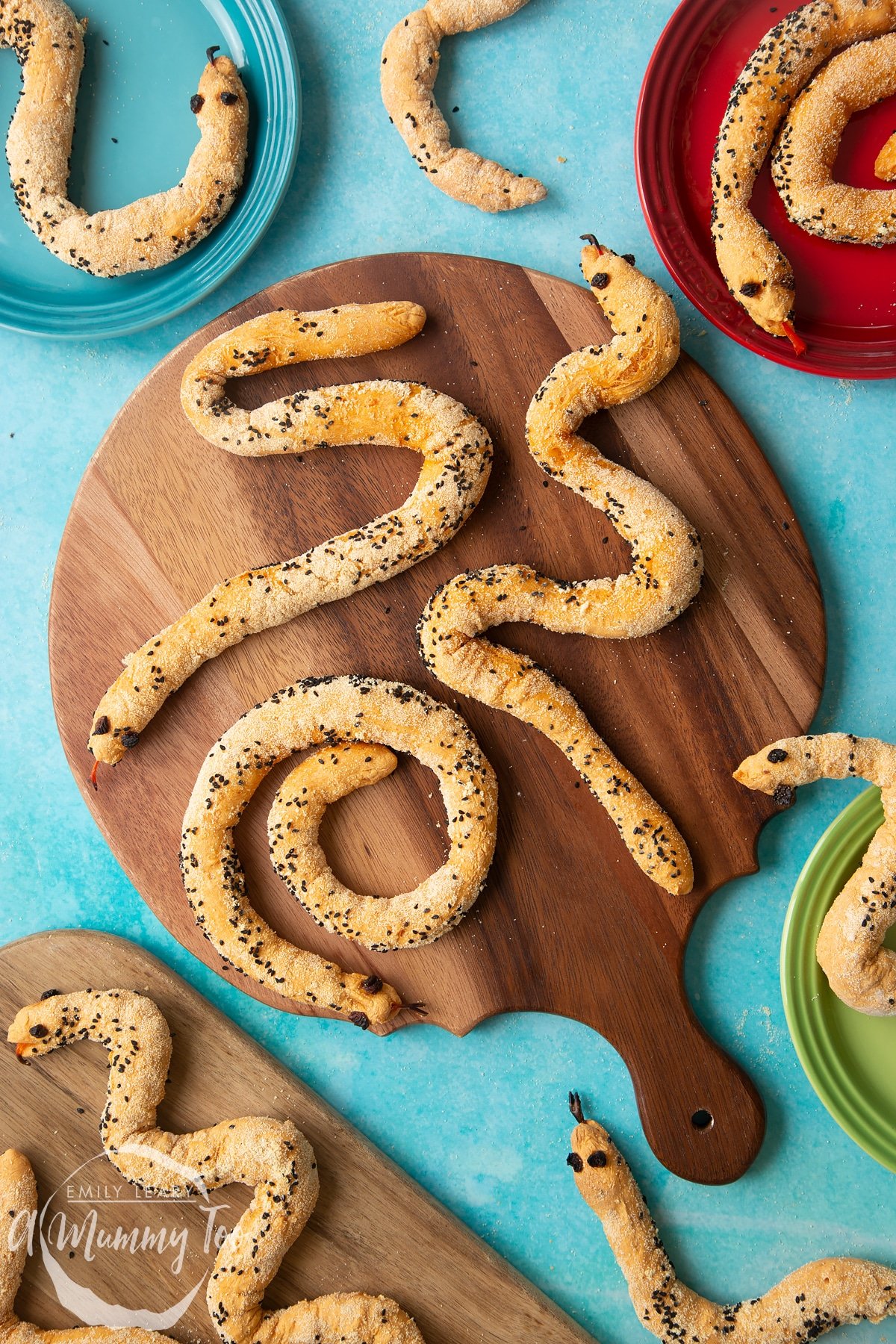 Bread snakes on a wooden board. More bread snakes are shown on coloured plates at the edges of the photo. each of the snakes wiggles in a different shape.