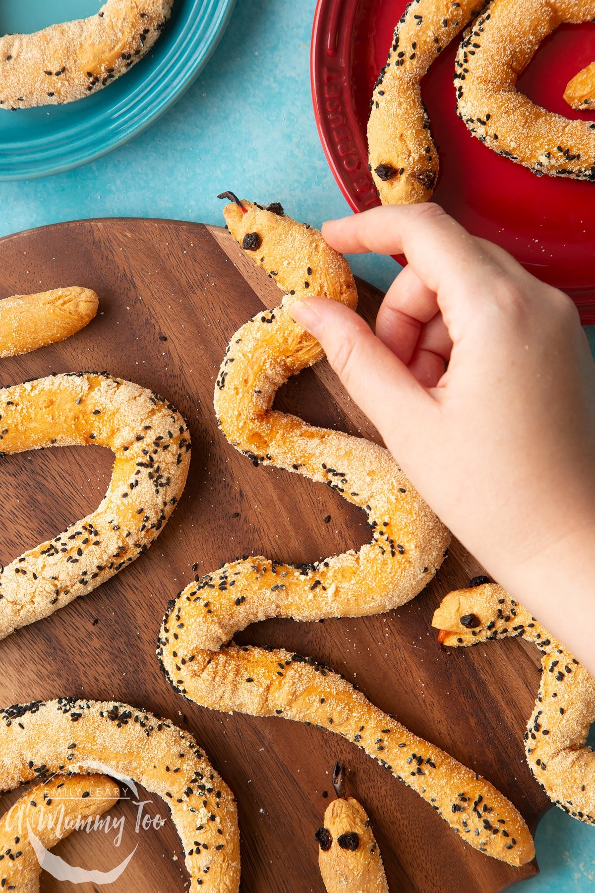 Bread snakes on a wooden board. A hand reaches for one, holding it near its head.