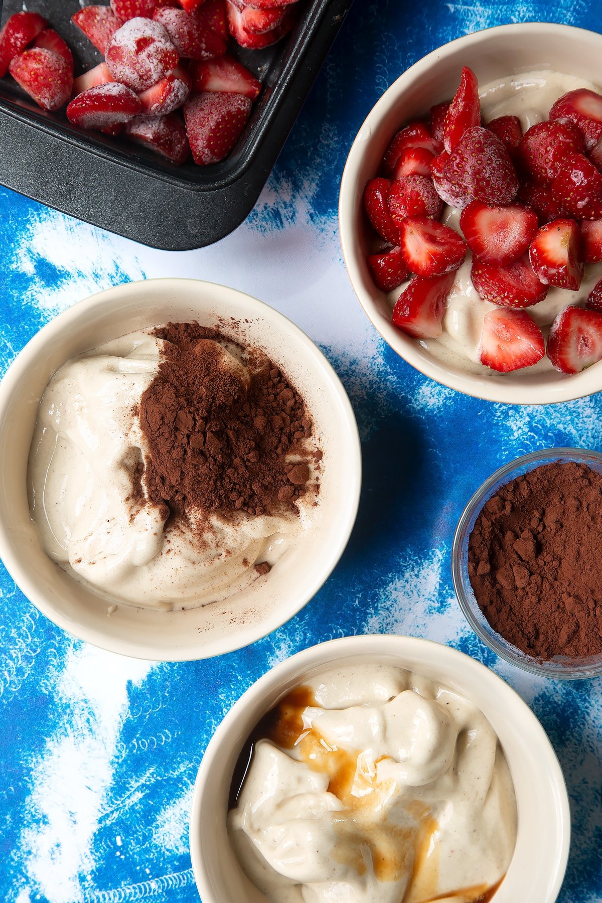 Pureed frozen bananas in three bowls. One has cocoa added, another vanilla and the third frozen strawberries.