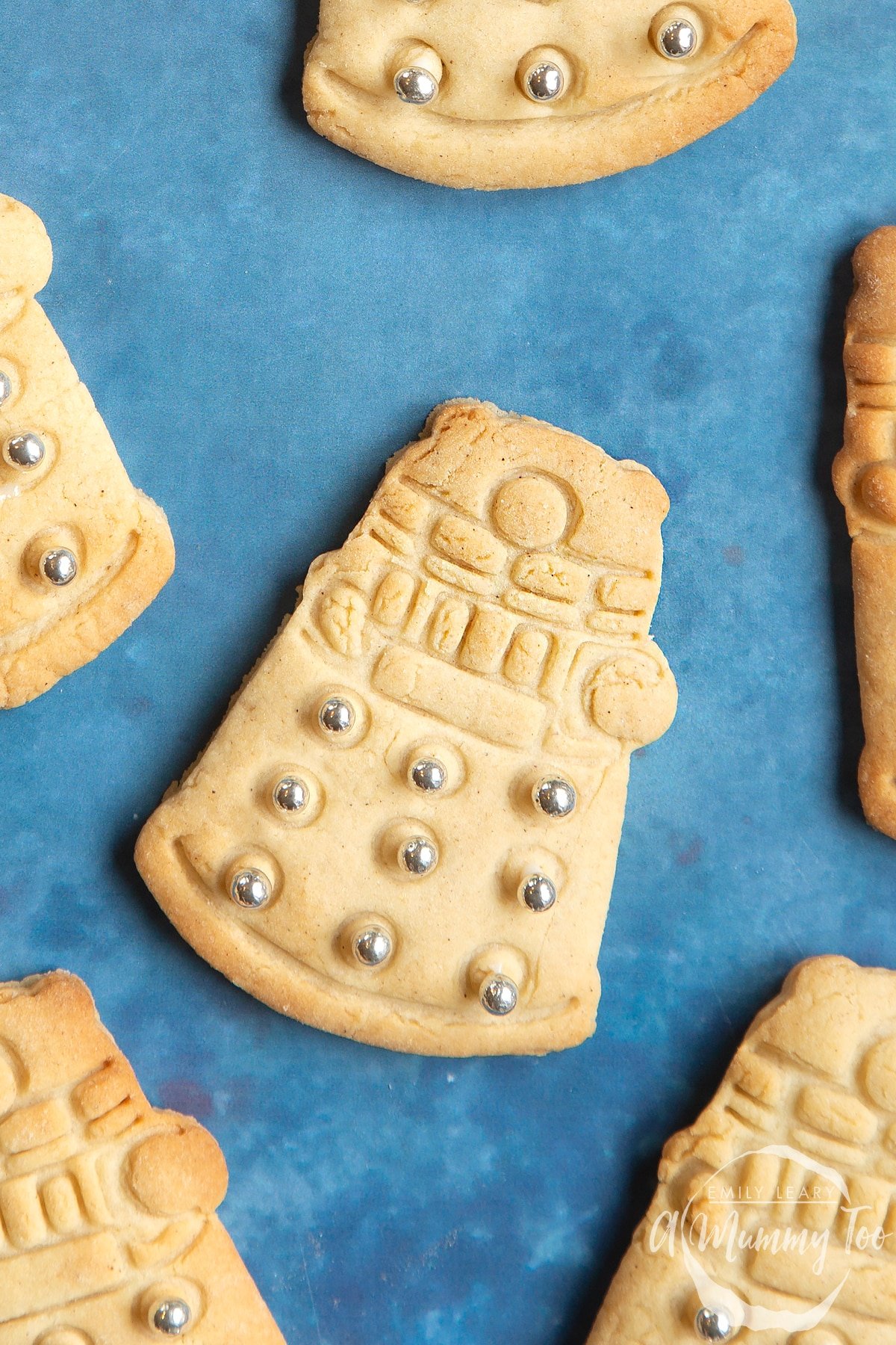 Close up of a Dalek cookies on a blue background. The cookie is decorated with edible silver candy balls. 