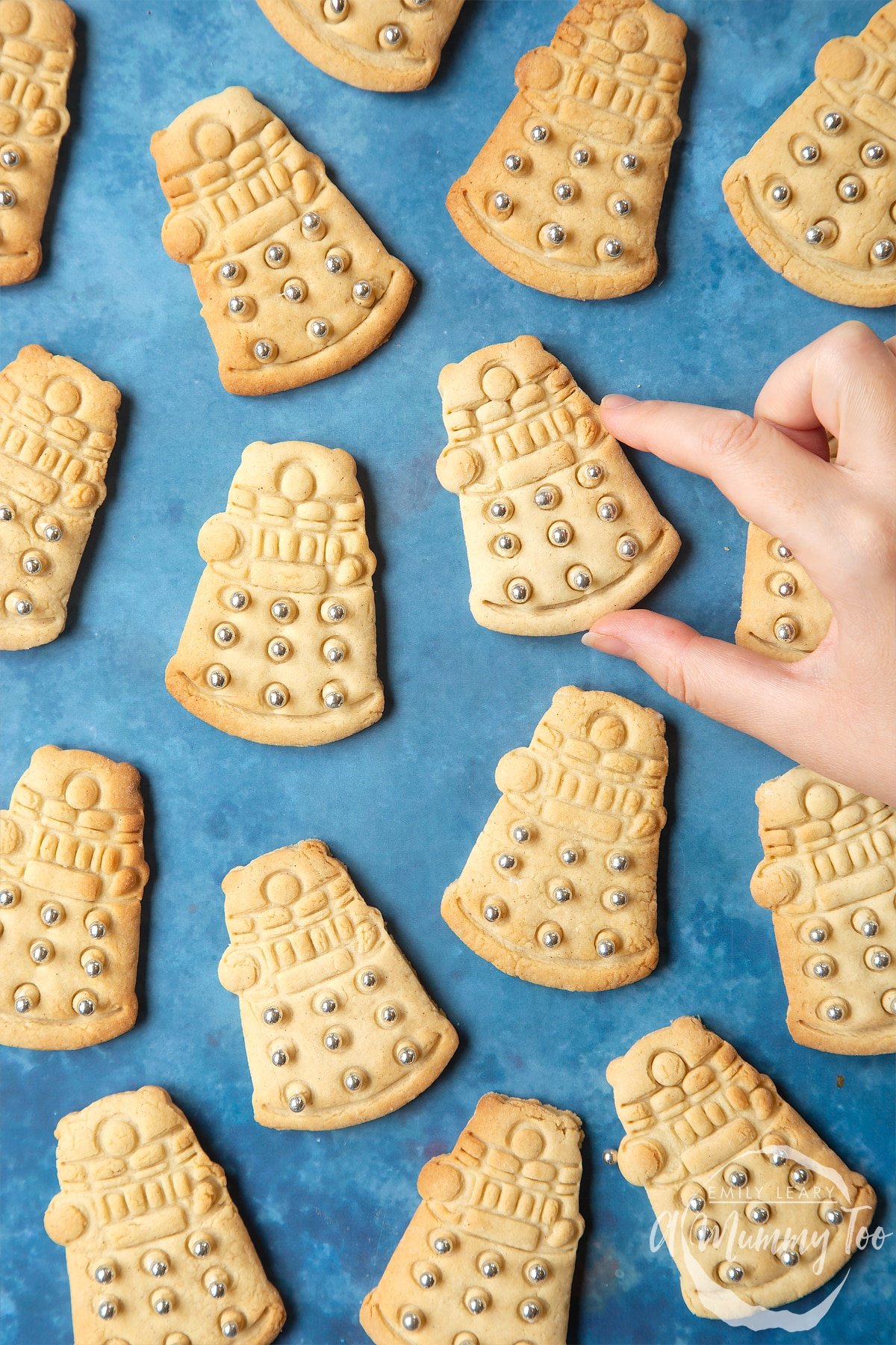 Dalek sugar cookies decorated with silver candy balls. A hand reaches for one.