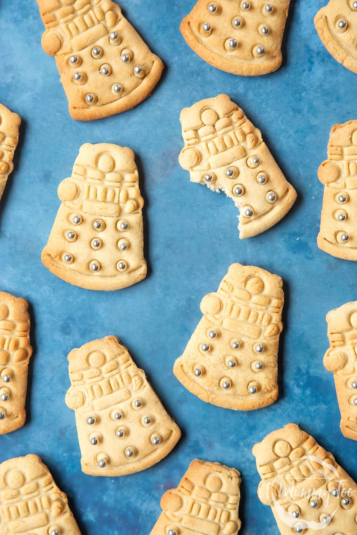 Dalek cookies on a blue background. The cookies are decorated with edible silver candy balls. One of the cookies has a bite out of it.