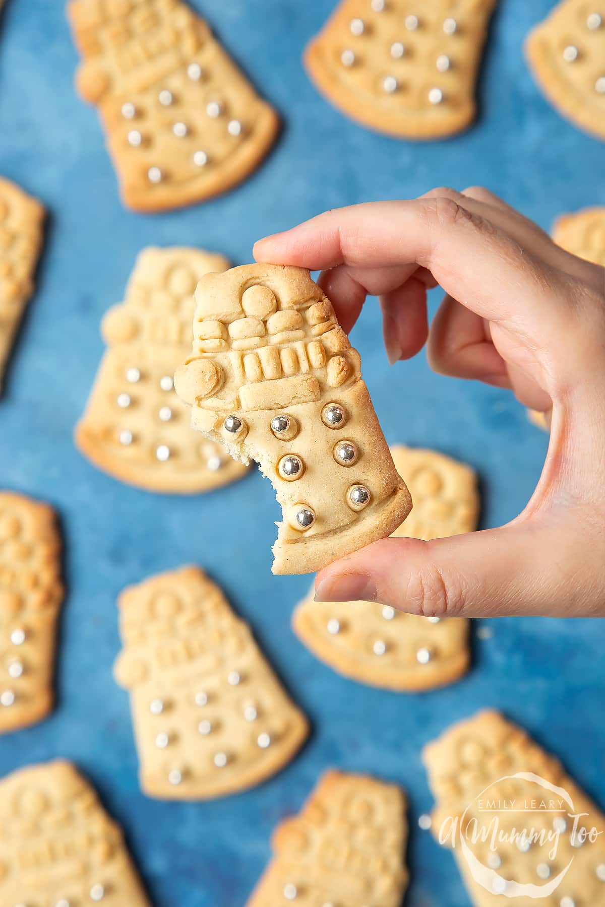 Dalek cookies on a blue background. The cookies are decorated with edible silver candy balls. A hand holds one of the cookies, which has a bite out of it.