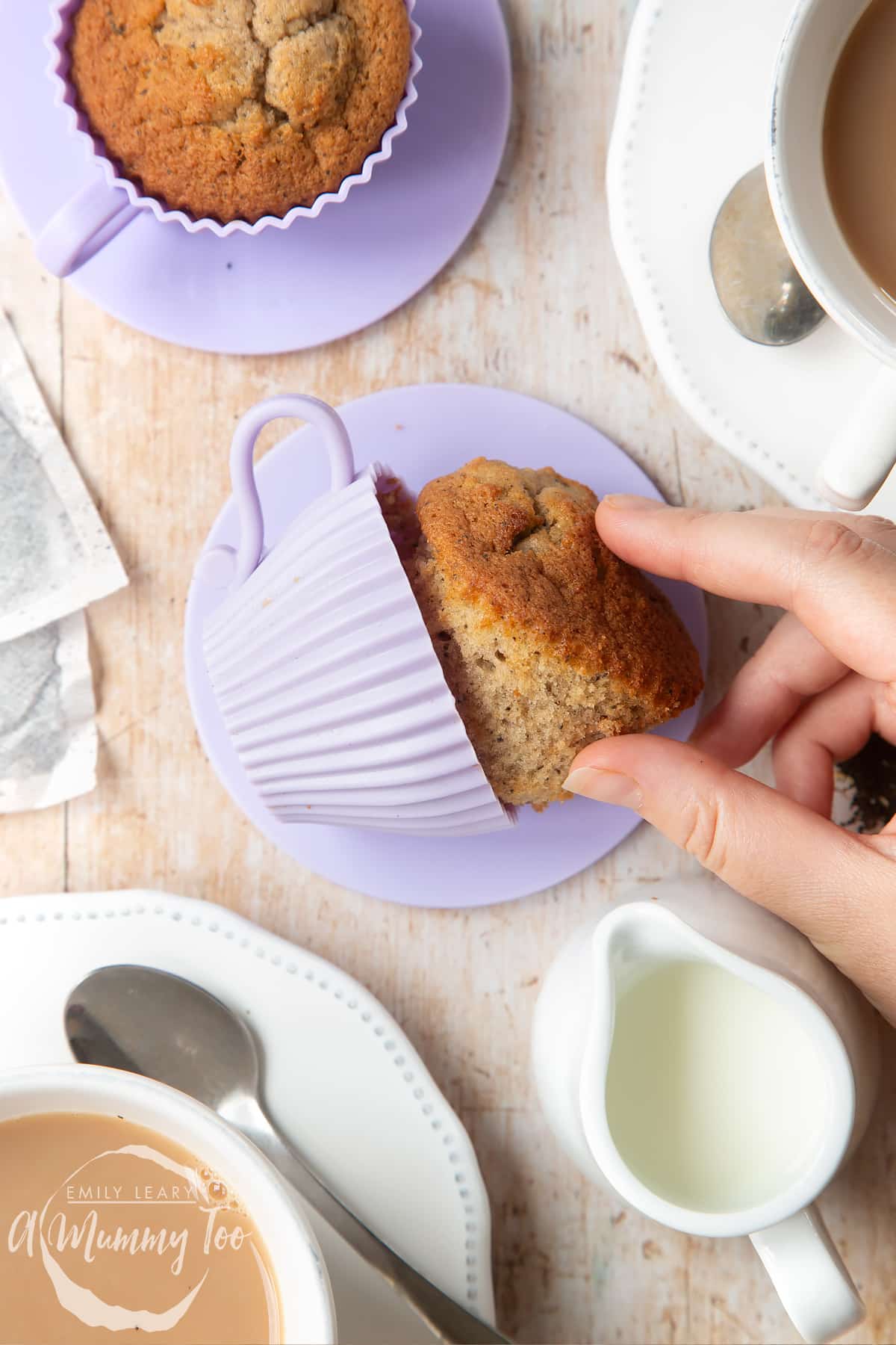 Overhead shot of a hand touching an Earl Grey cupcake served on a silicone casing with a mummy too logo in the lower-left corner