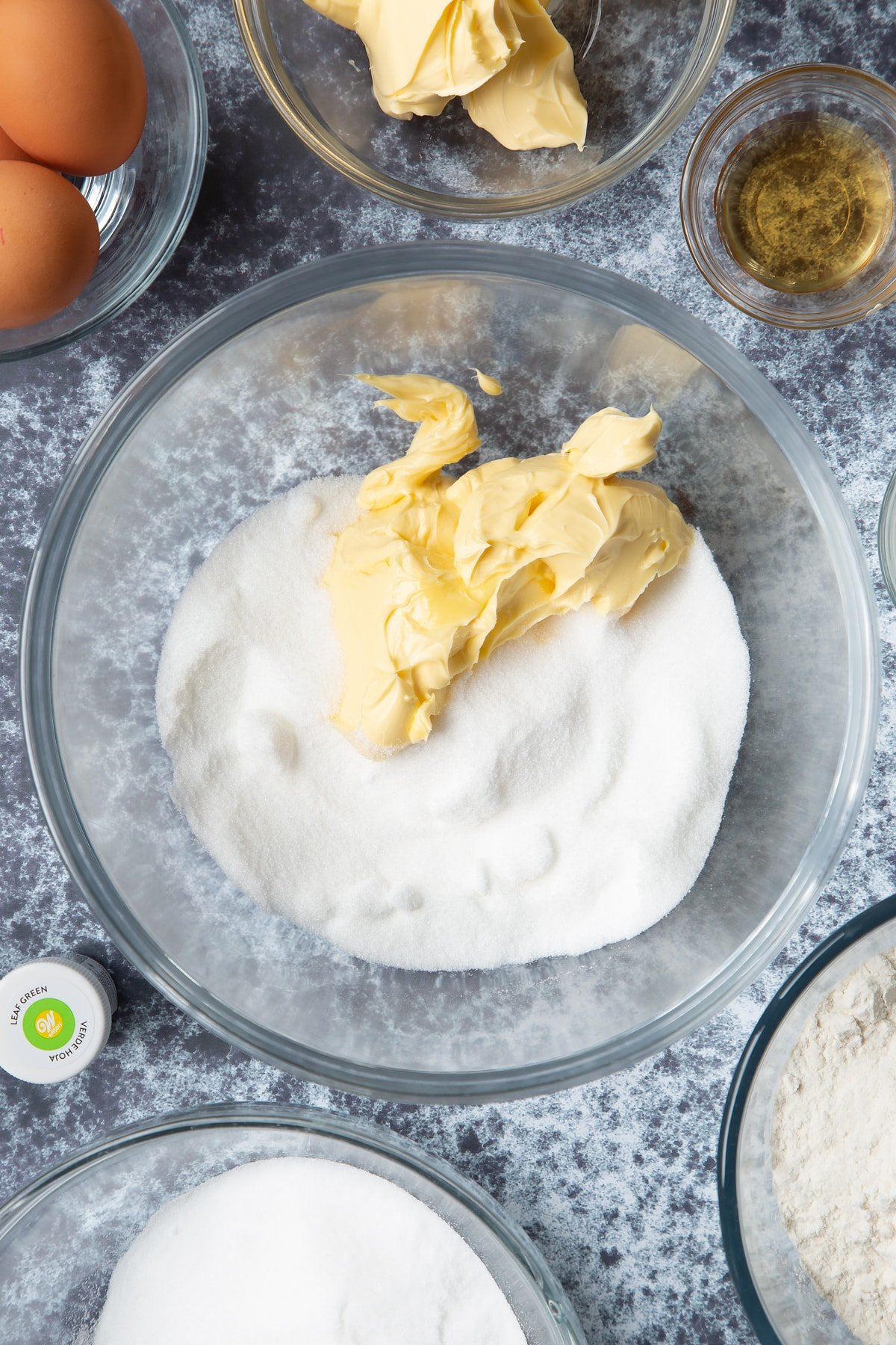 Sugar and margarine in a large mixing bowl. Ingredients to make green monster cakes surround the bowl. 