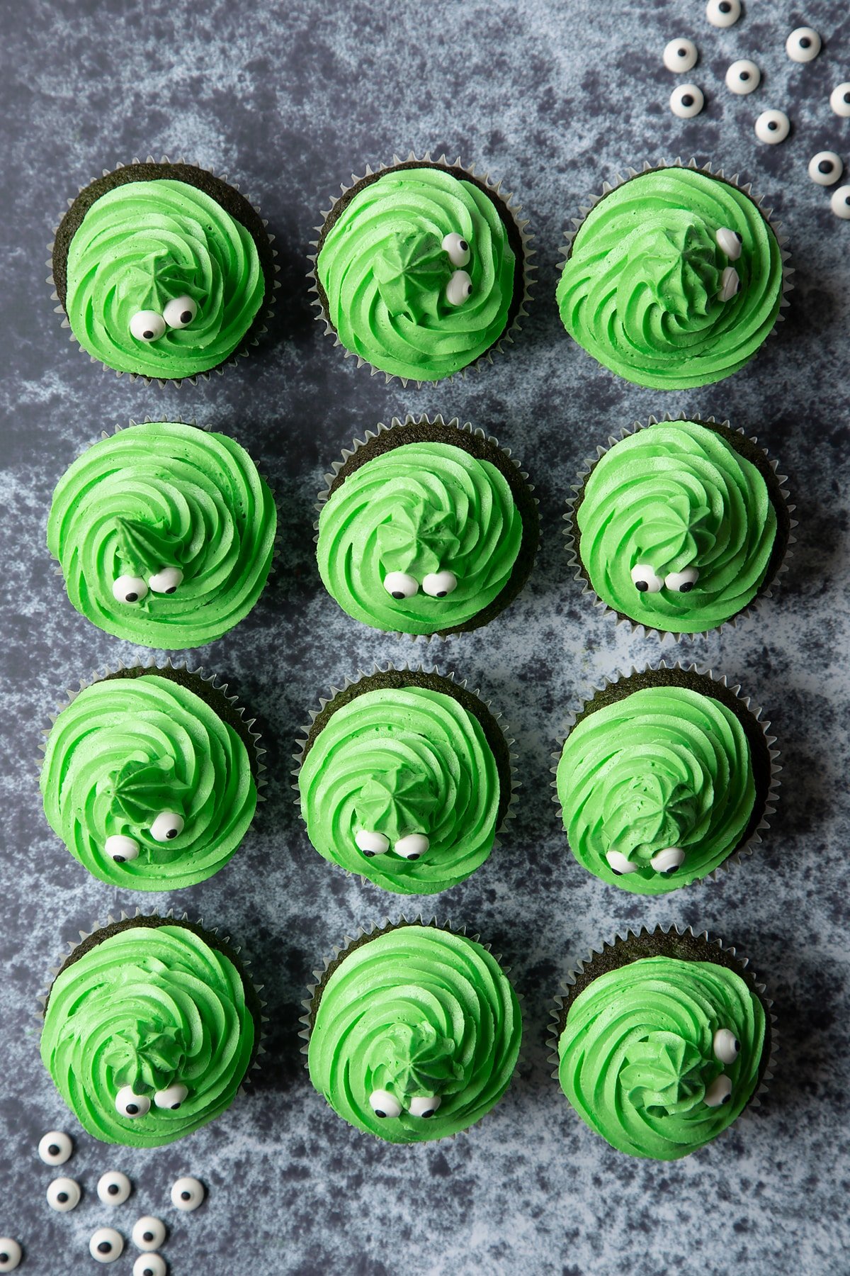 Green vanilla chocolate chip cupcakes decorated with swirls of green peppermint frosting and candy eyeballs to look like green monster cakes.