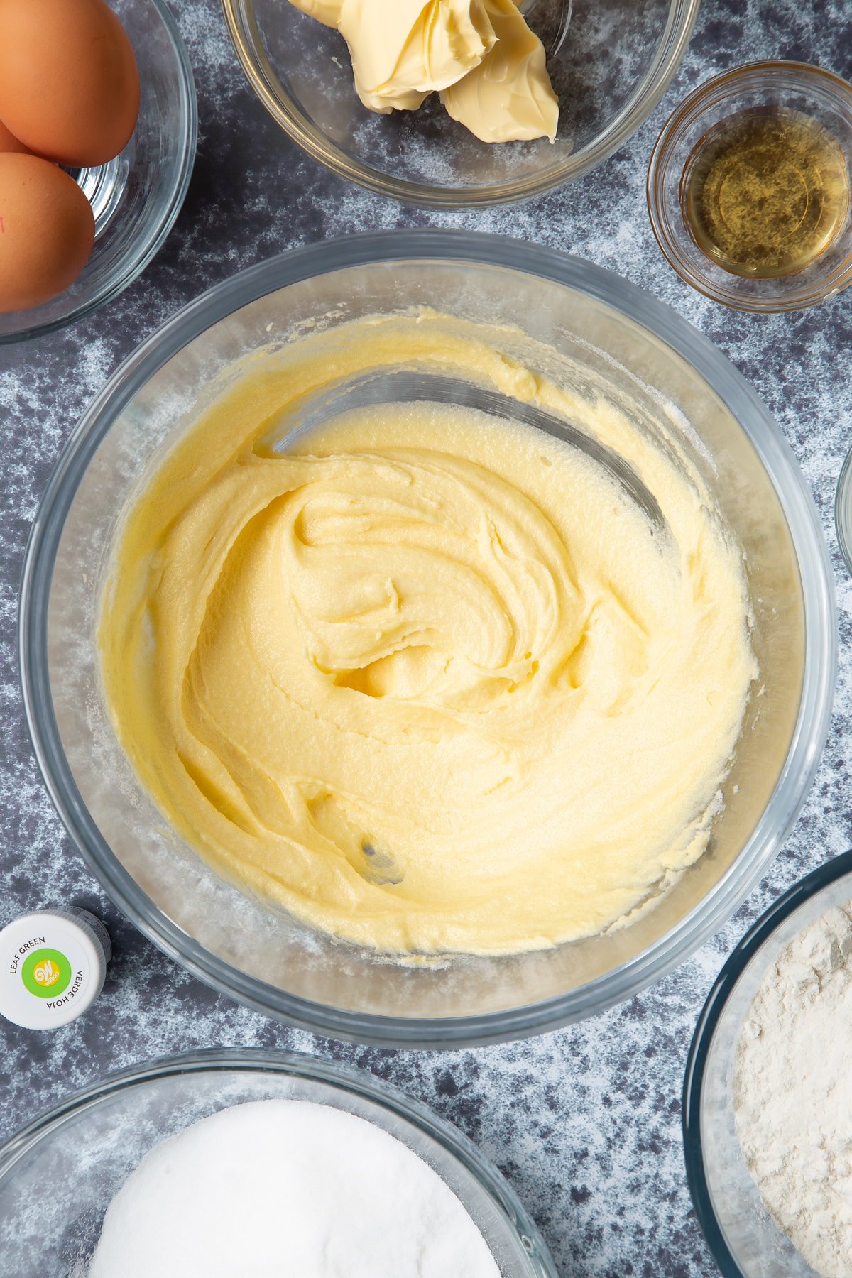 Sugar and margarine beaten together in a large mixing bowl. Ingredients to make green monster cakes surround the bowl. 