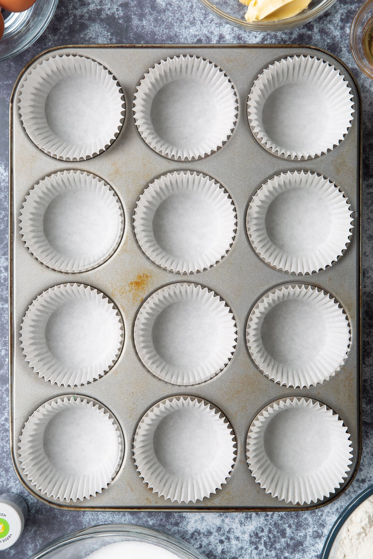 12 hole muffin tray lined with cupcake cases. Ingredients to make green monster cakes surround the tray.