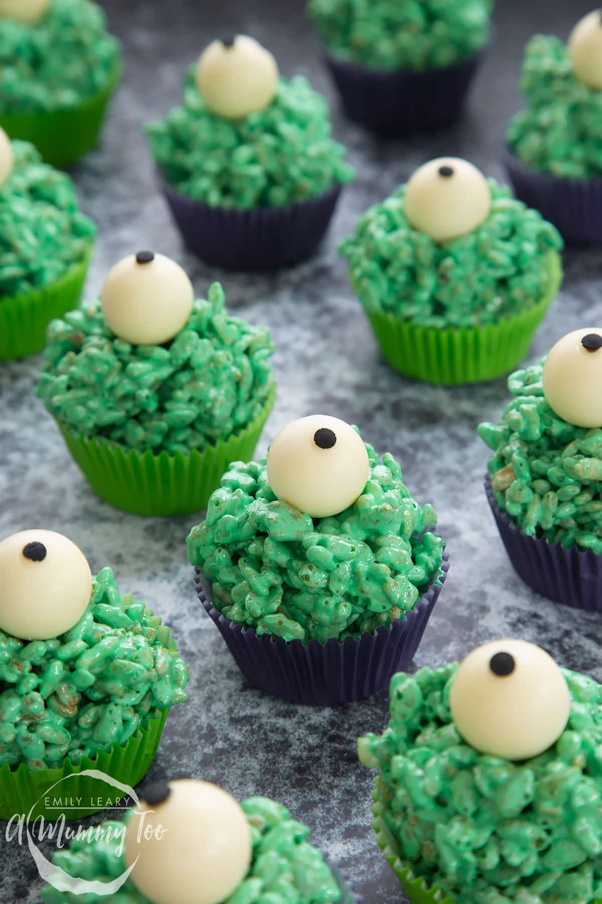 Halloween crispy cakes in purple and green cupcake cases. The crispy cakes are dyed green and topped with white chocolate spheres decorated to look like eyeballs.