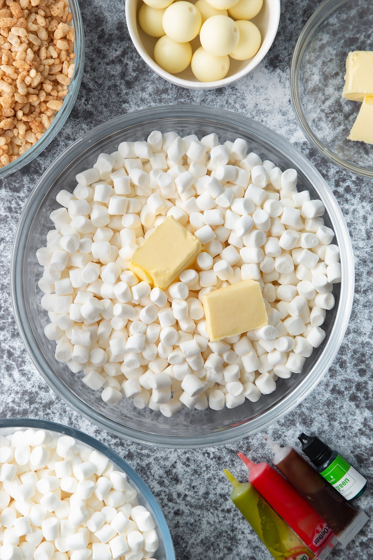 Mini marshmallows and cubes of butter in a large mixing bowl. Ingredients to make Halloween crispy cakes surround the bowl.