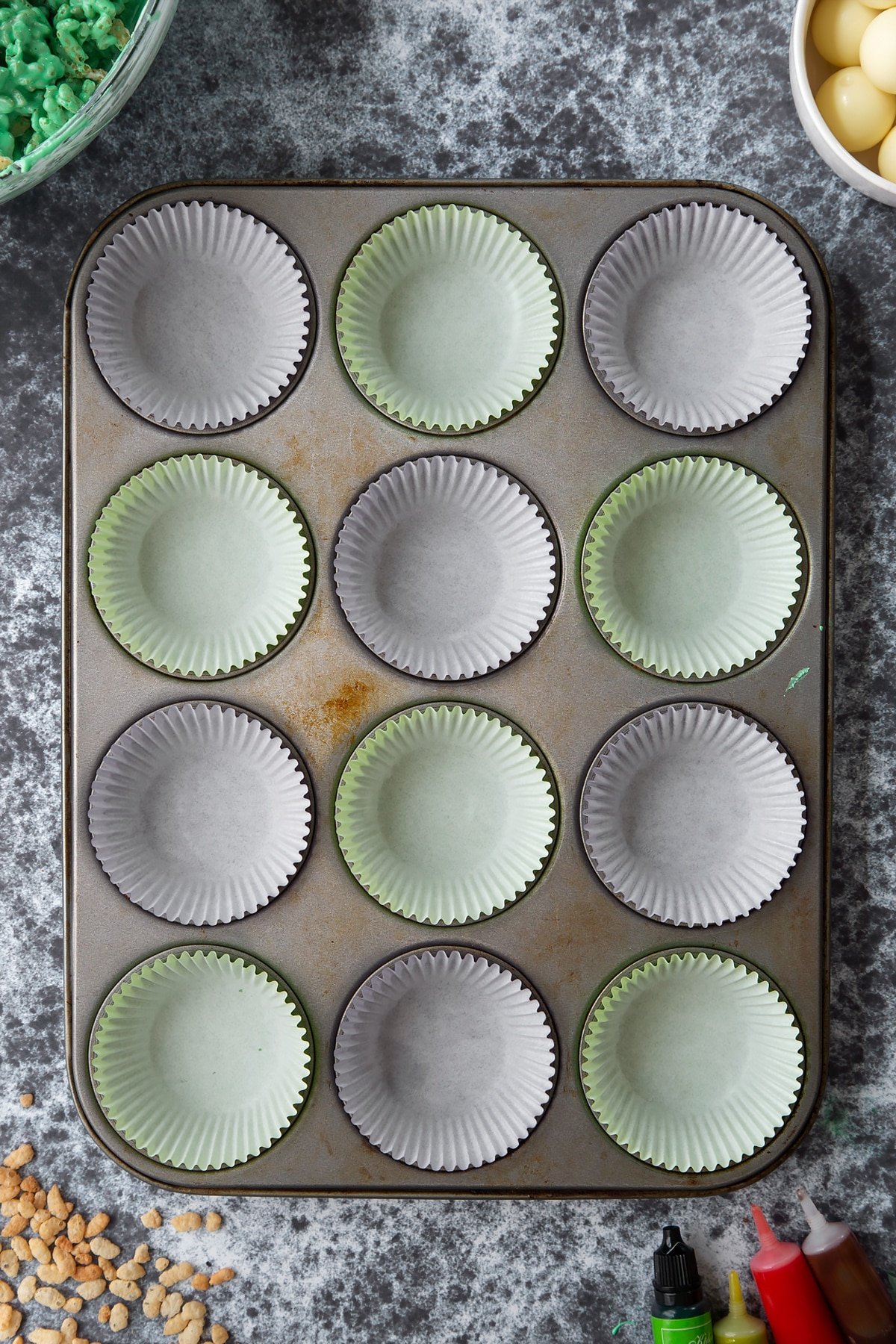 12-hole muffin tray lined with cupcake cases. Ingredients to make Halloween crispy cakes surround the tray.