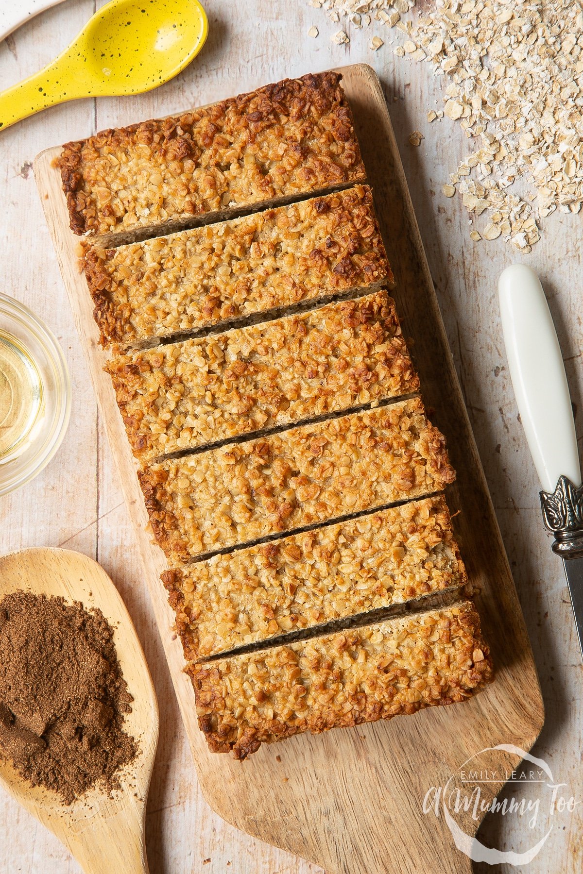 Overhead shot of sliced vanilla oat bars fruity flapjacks served on a wooden plate with a mummy too logo in the lower-right corner