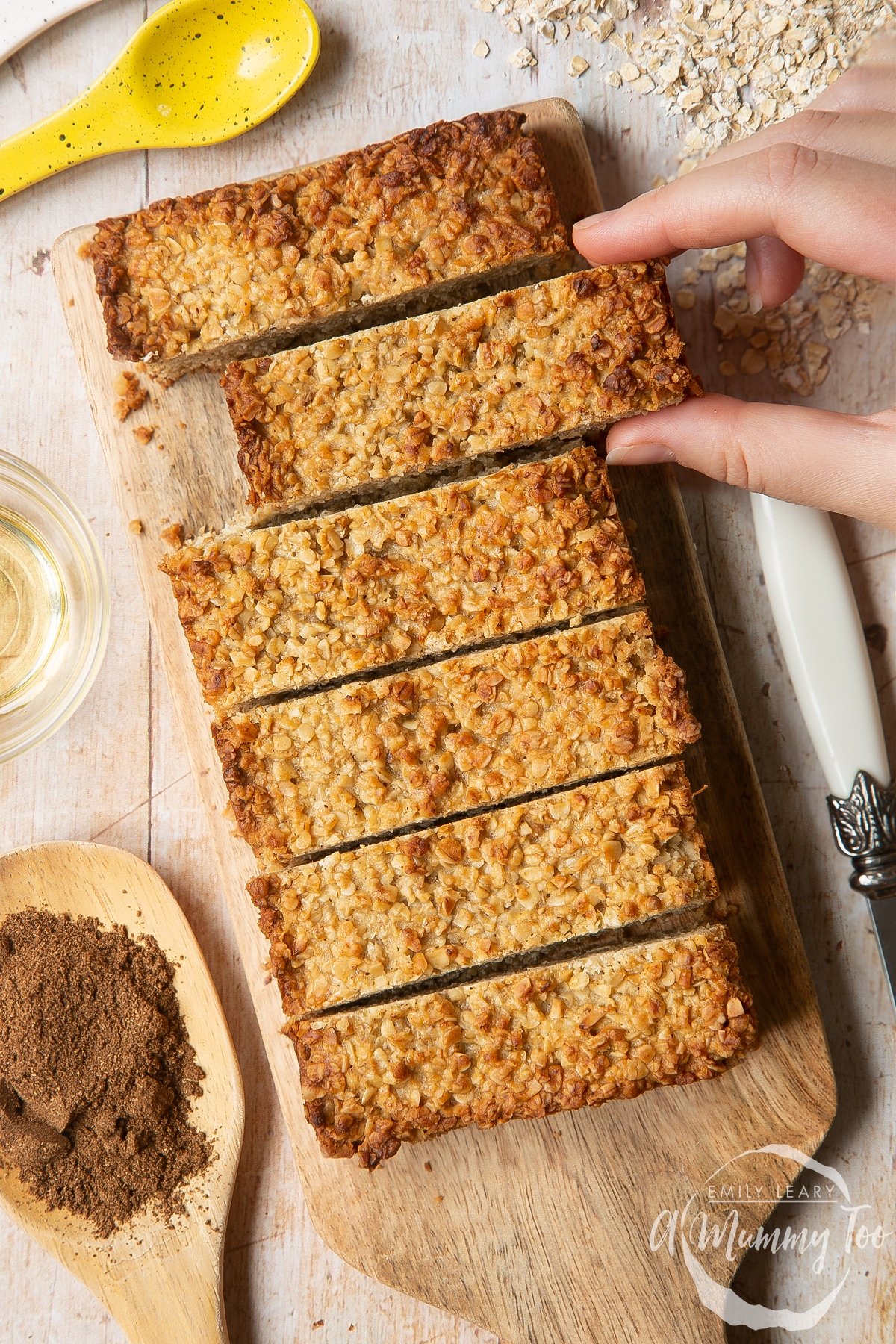 Overhead shot of a hand picking up lower sugar flapjacks served on a wooden plate with a mummy too logo in the lower-right corner