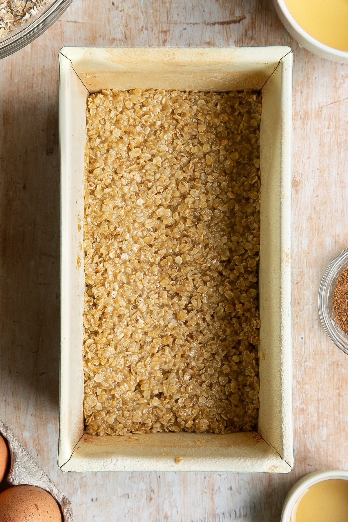 Overhead shot of flattened vanilla oats mix in a greased loaf tin