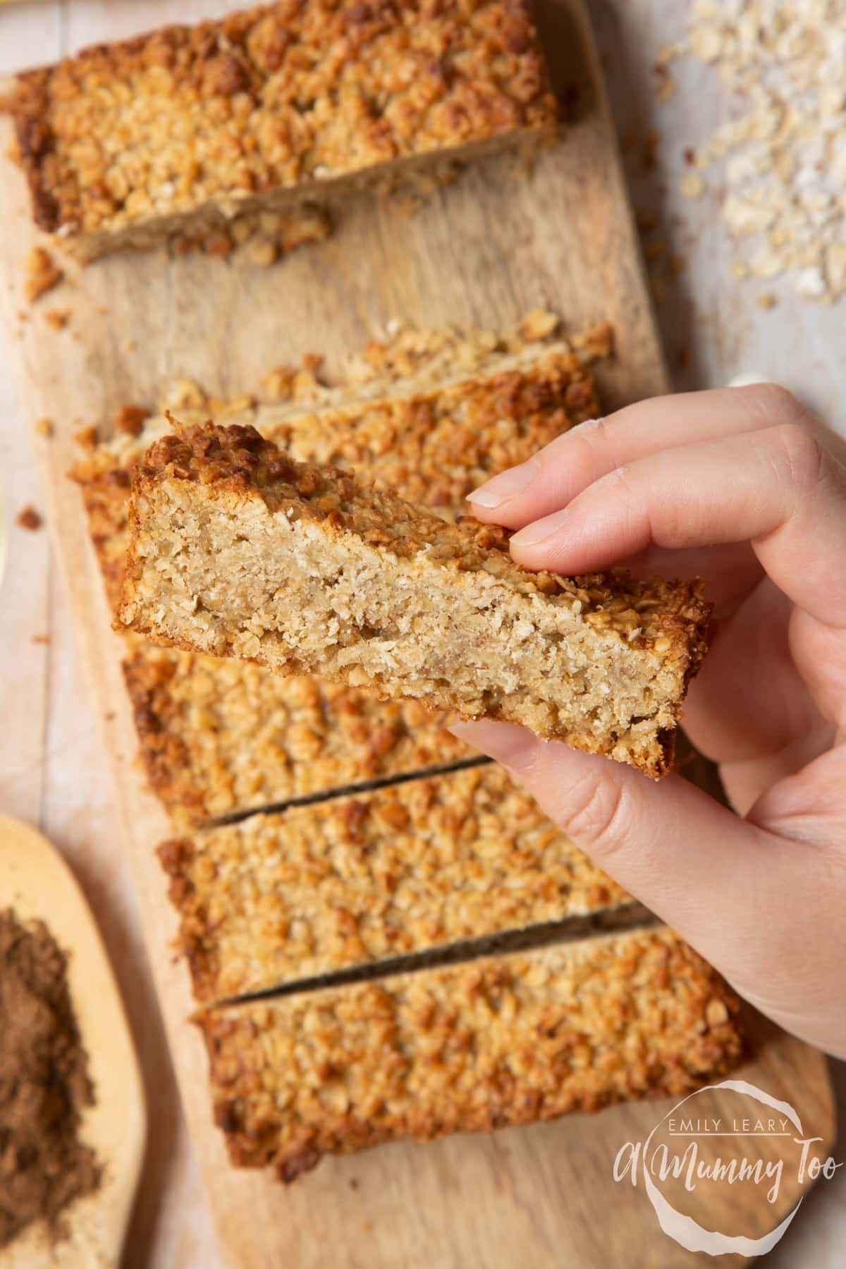 Front angle shot of a hand holding a fruity low gi vanilla oat flapjack with a mummy too logo in the lower-right corner