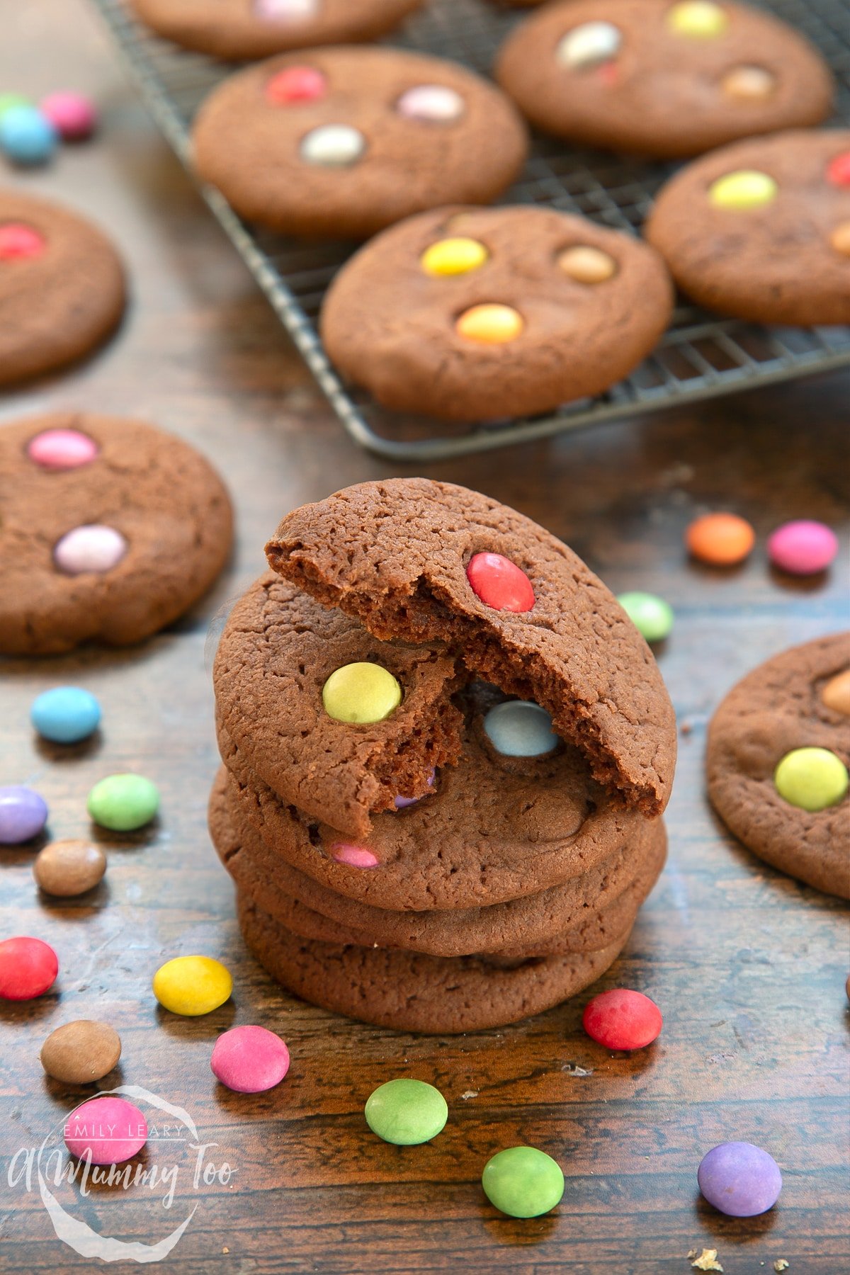 Smartie cookies stacked up on a dark wooden surface. The top cookie has been broken in two.