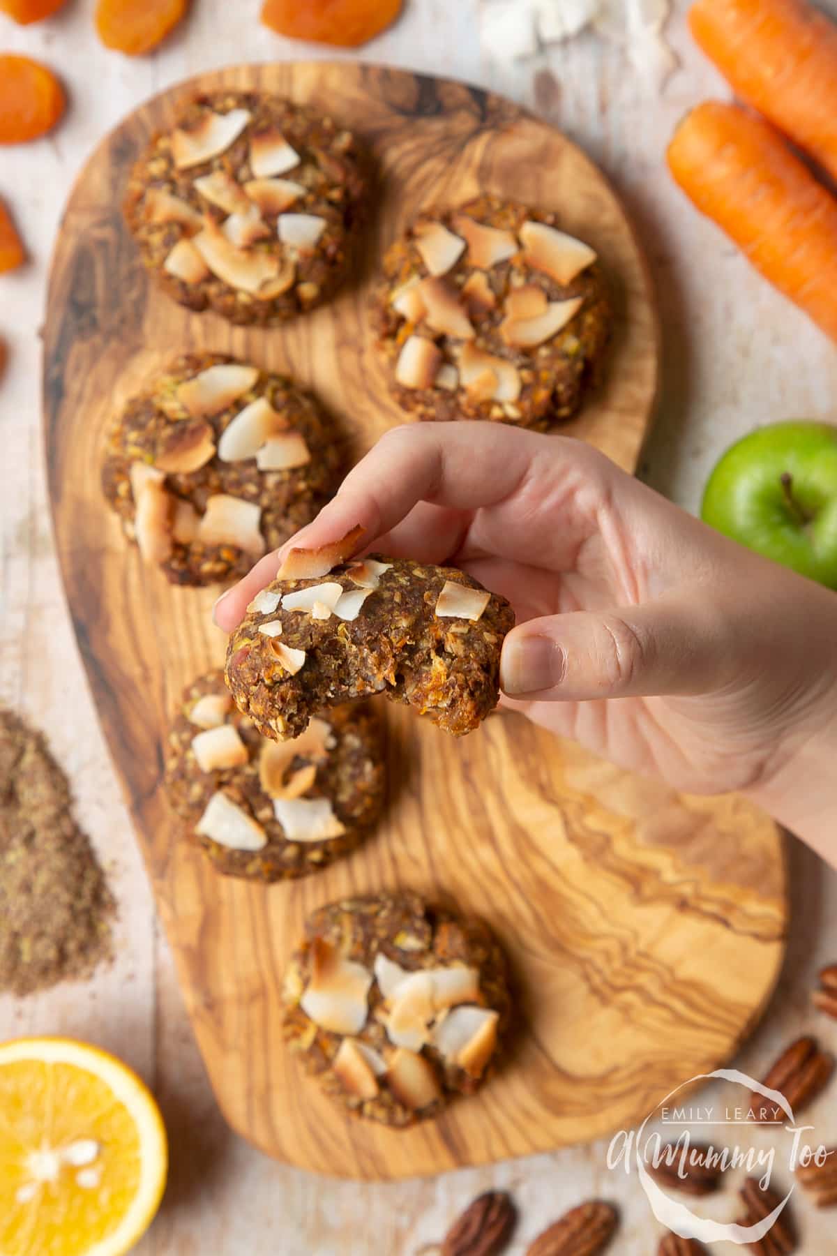 Front angle shot of a hand holding Superfood breakfast cookies served on a wooden board with a mummy too logo in the lower-left corner