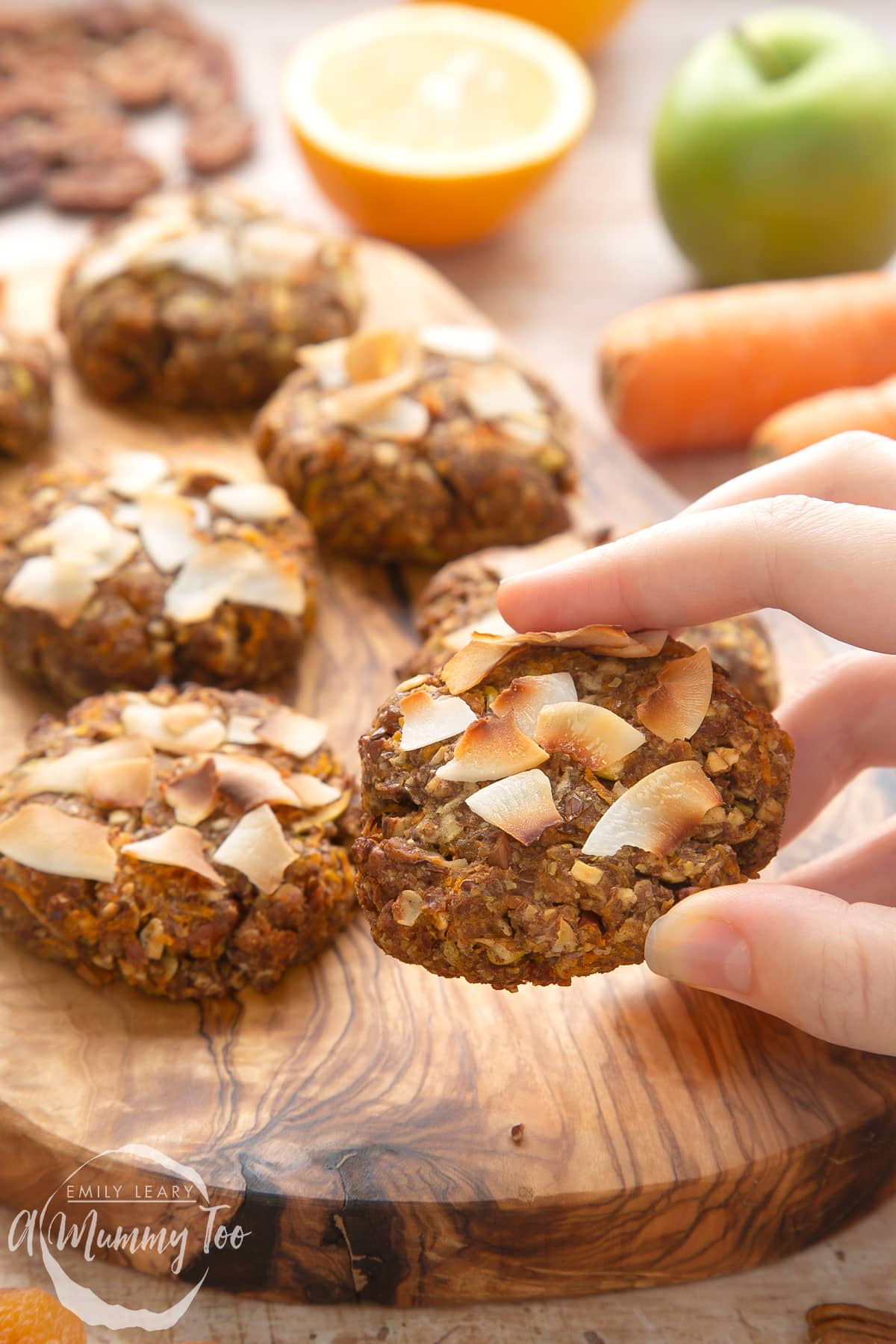 Front angle shot of a hand holding Superfood breakfast cookies served on a wooden board with a mummy too logo in the lower-left corner