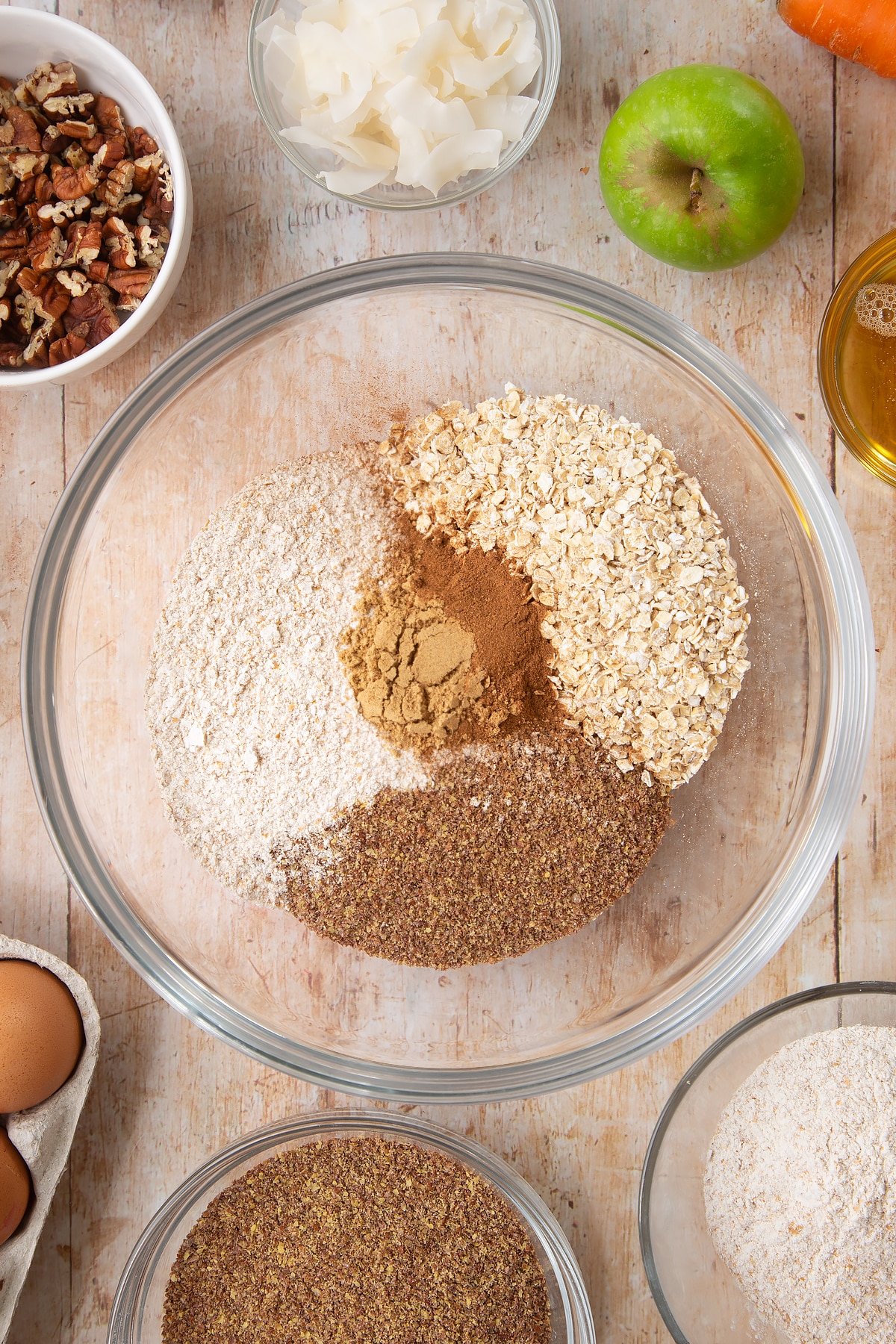 Overhead shot of flour, oats, baking powder, ginger and cinnamon in a large clear bowl