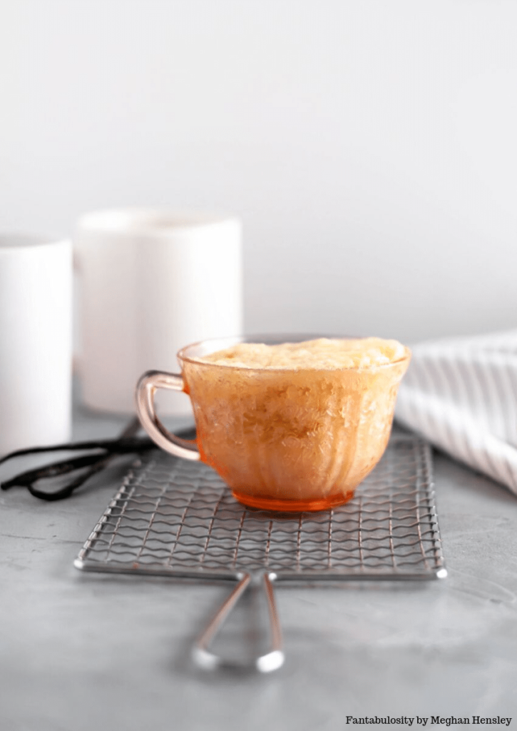 Vanilla mug cake, made in a transparent teacup, standing on a small cooling rack.