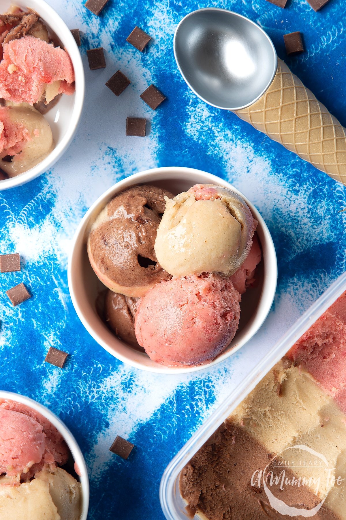 Dairy-free Neapolitan ice cream served in a small white bowl. An ice cream scoop and scattered chocolate chips are also shown.