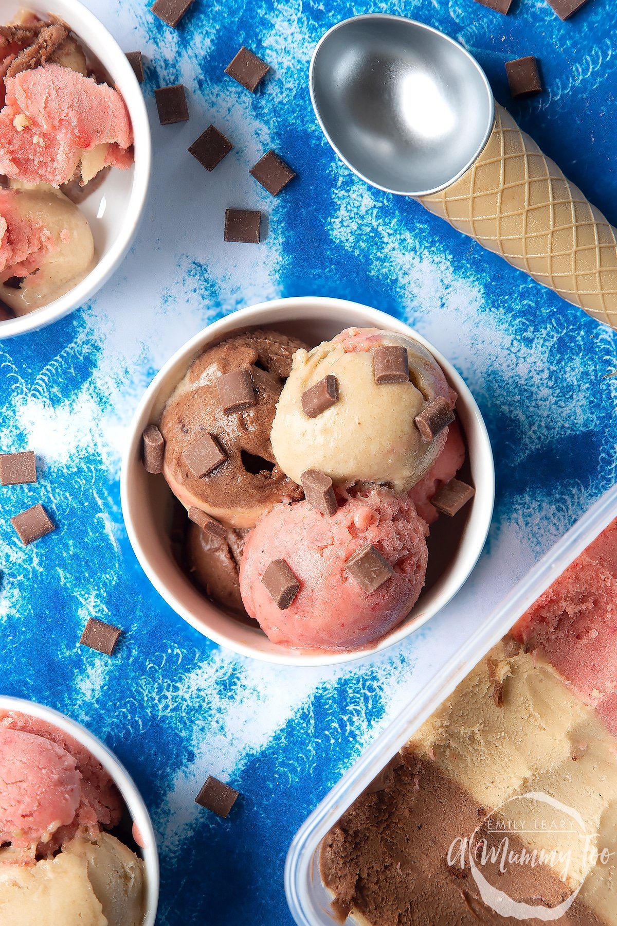 Dairy-free Neapolitan ice cream served in a small white bowl, topped with chocolate chips. An ice cream scoop and scattered chocolate chips are also shown.
