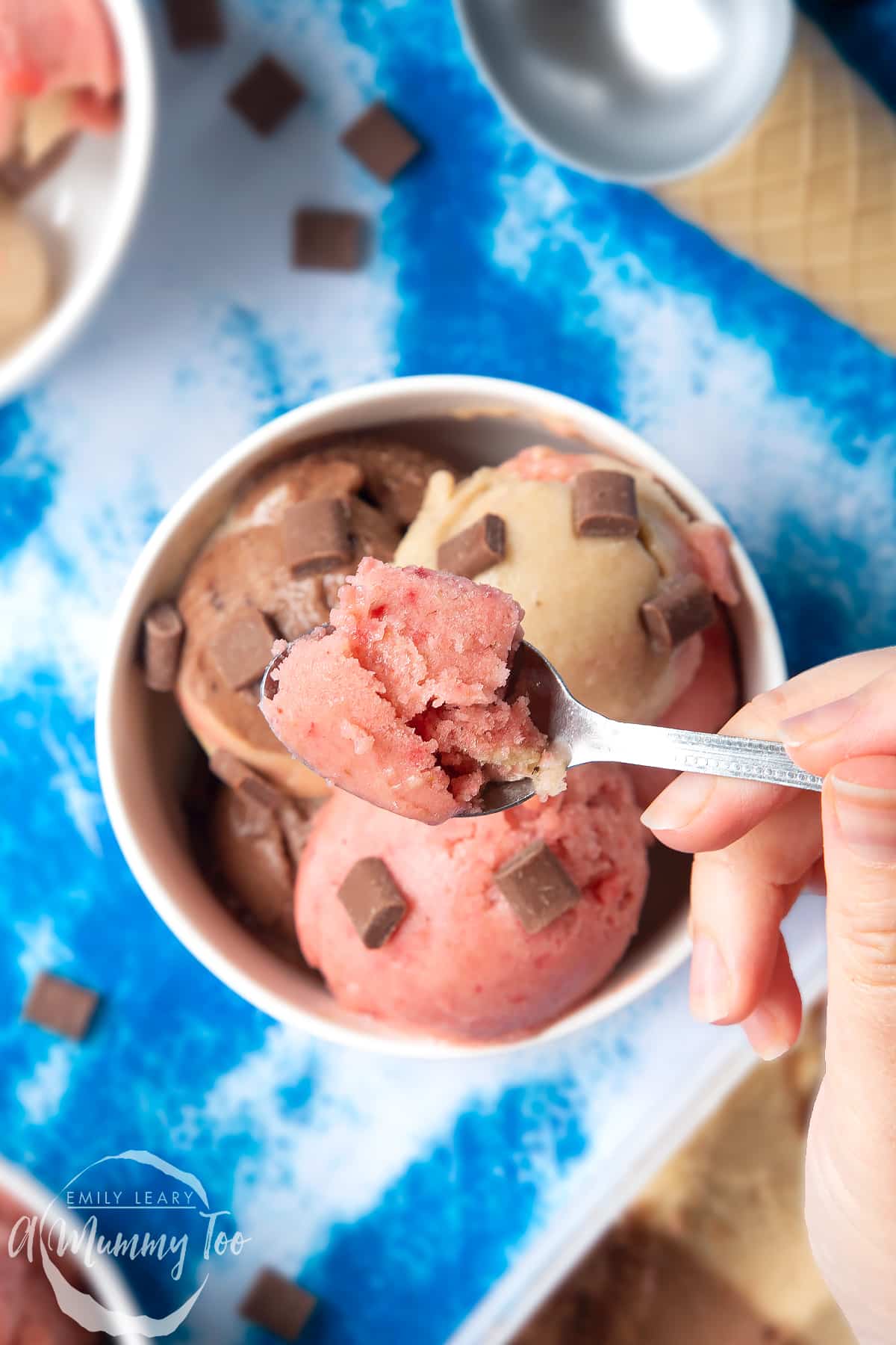 Dairy-free Neapolitan ice cream served in a small white bowl. A hand holds a spoon with some strawberry ice cream on it.