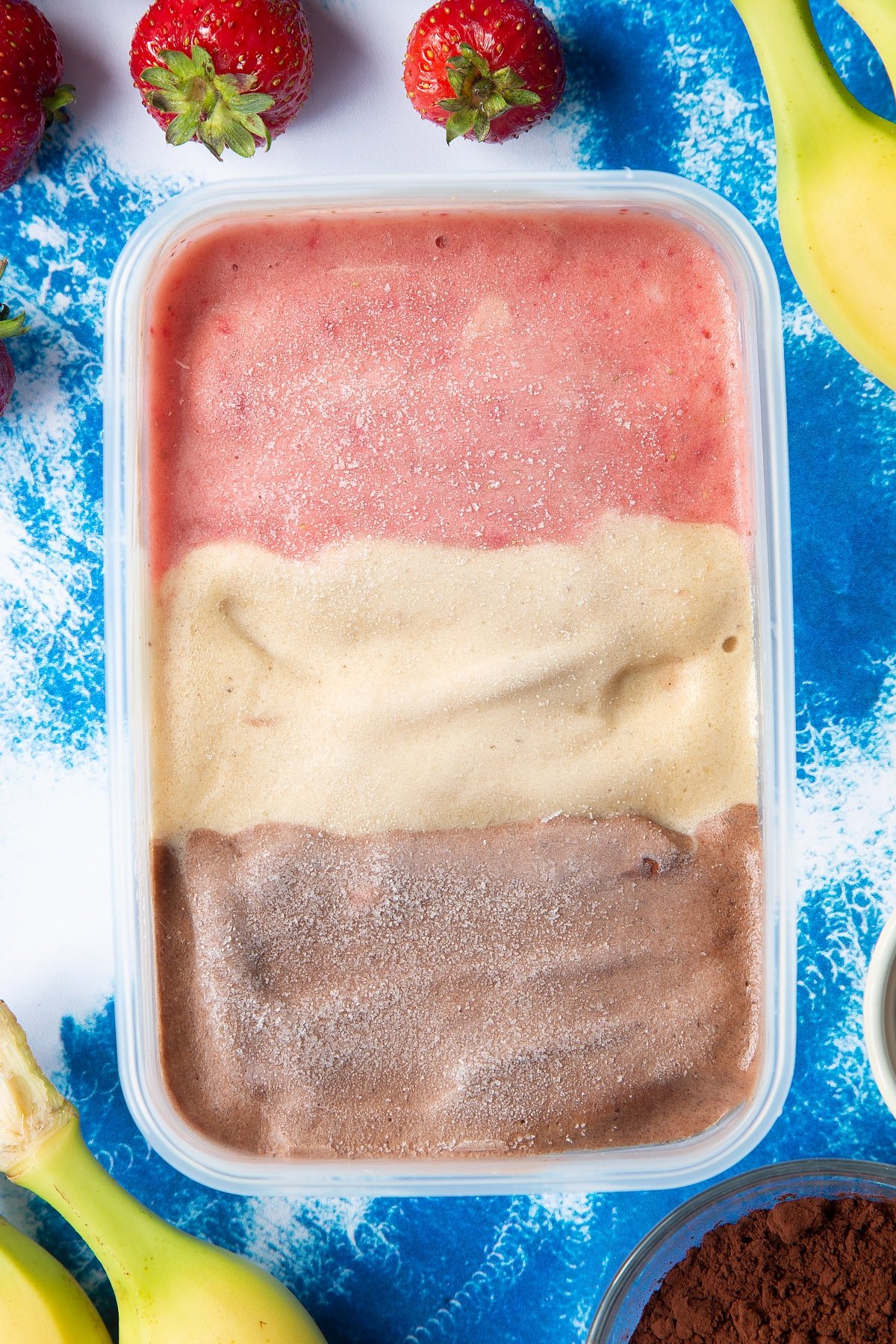 Dairy free Neapolitan ice cream in a tub in three layers - one chocolate, one vanilla and one strawberry.