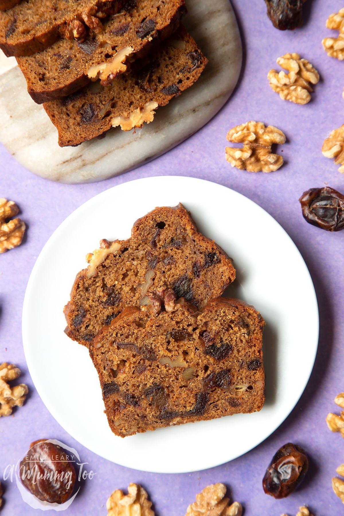 Overhead shot of vegan teabread served in a marble board with a mummy too logo in the lower-left corner