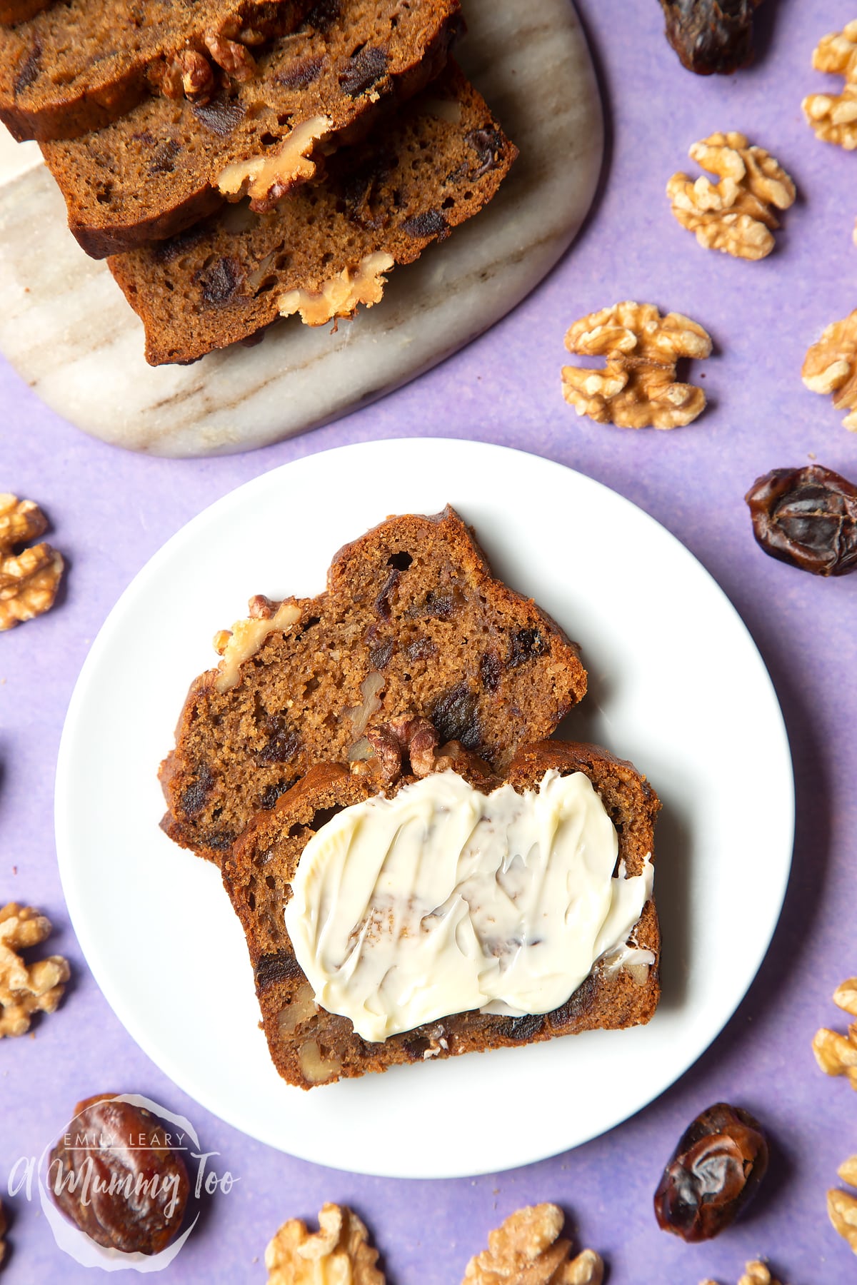 Overhead shot of vegan teabread slices served in a marble board with a mummy too logo in the lower-left corner