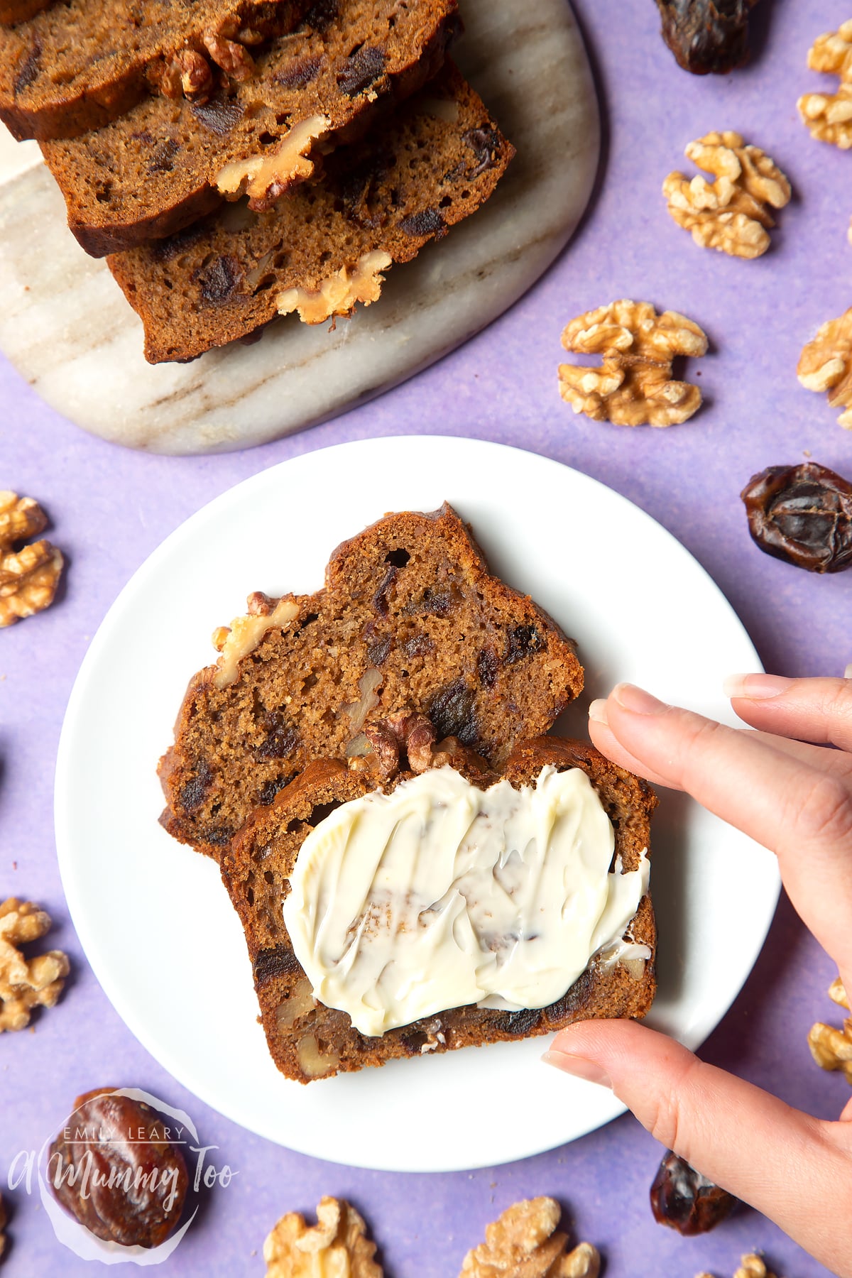 Overhead shot of vegan date teabread served in a marble board with a mummy too logo in the lower-left corner