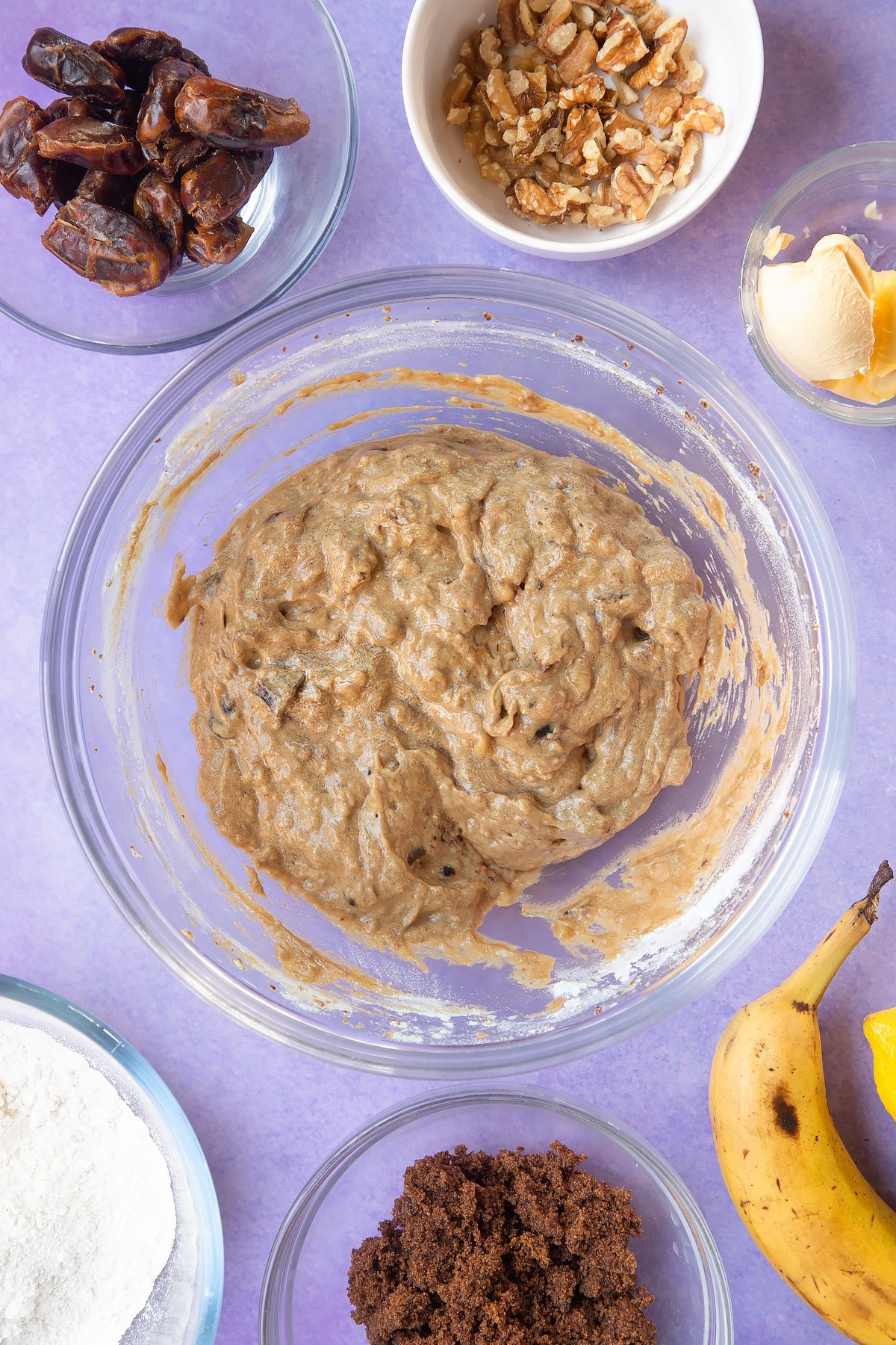 Overhead shot of soaked date mixture, banana mix, and flour in clear bowl
