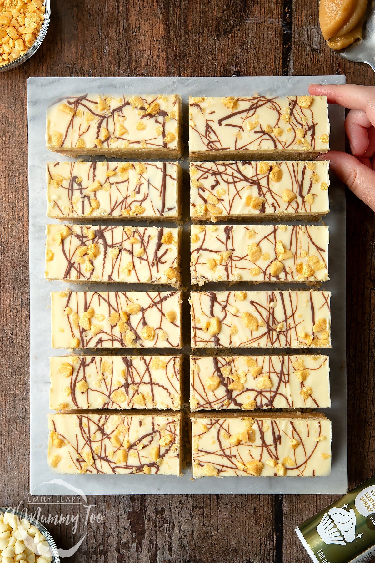 Overhead shot of a hand touching white chocolate shortbread with a mummy too logo in the lower-left corner