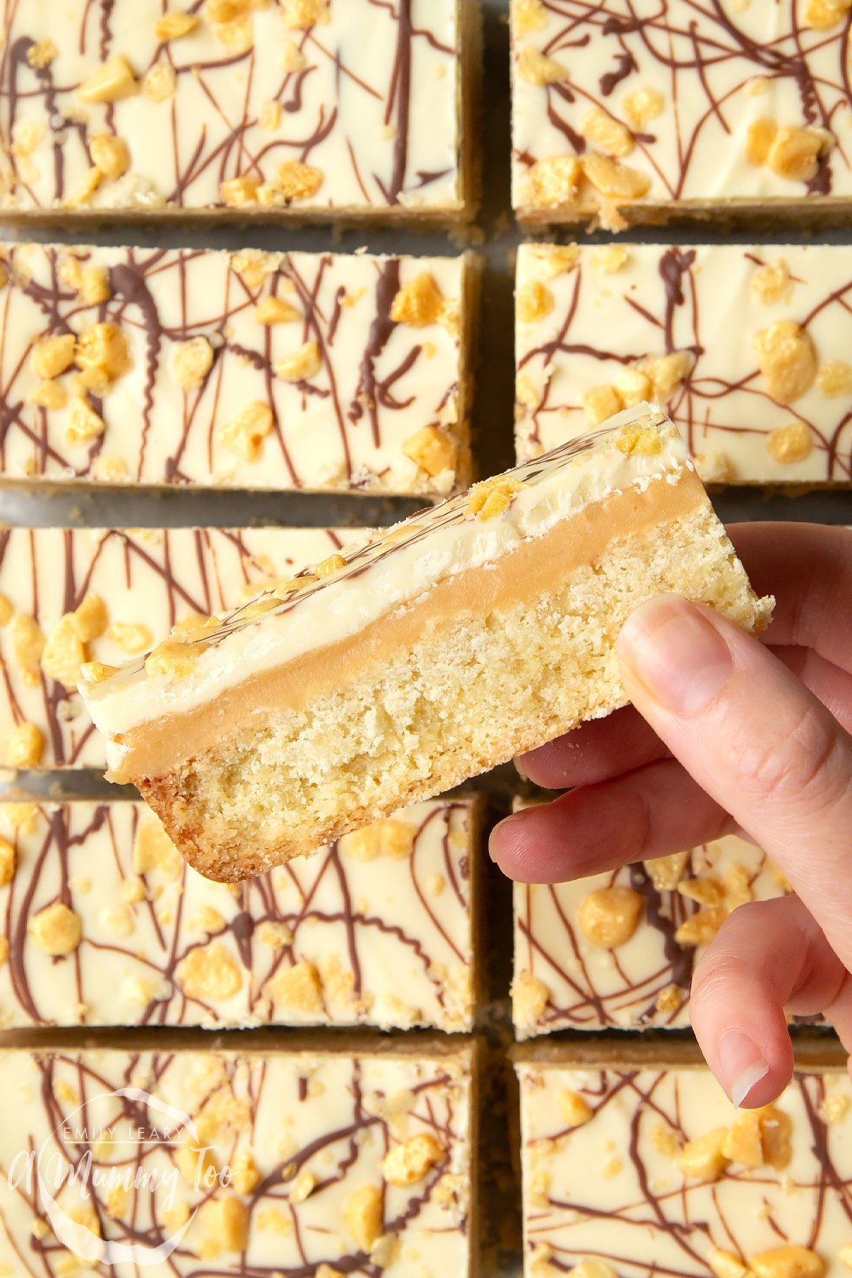 Front angle shot of a hand holding a White chocolate shortbread with a mummy too logo in the lower-left corner