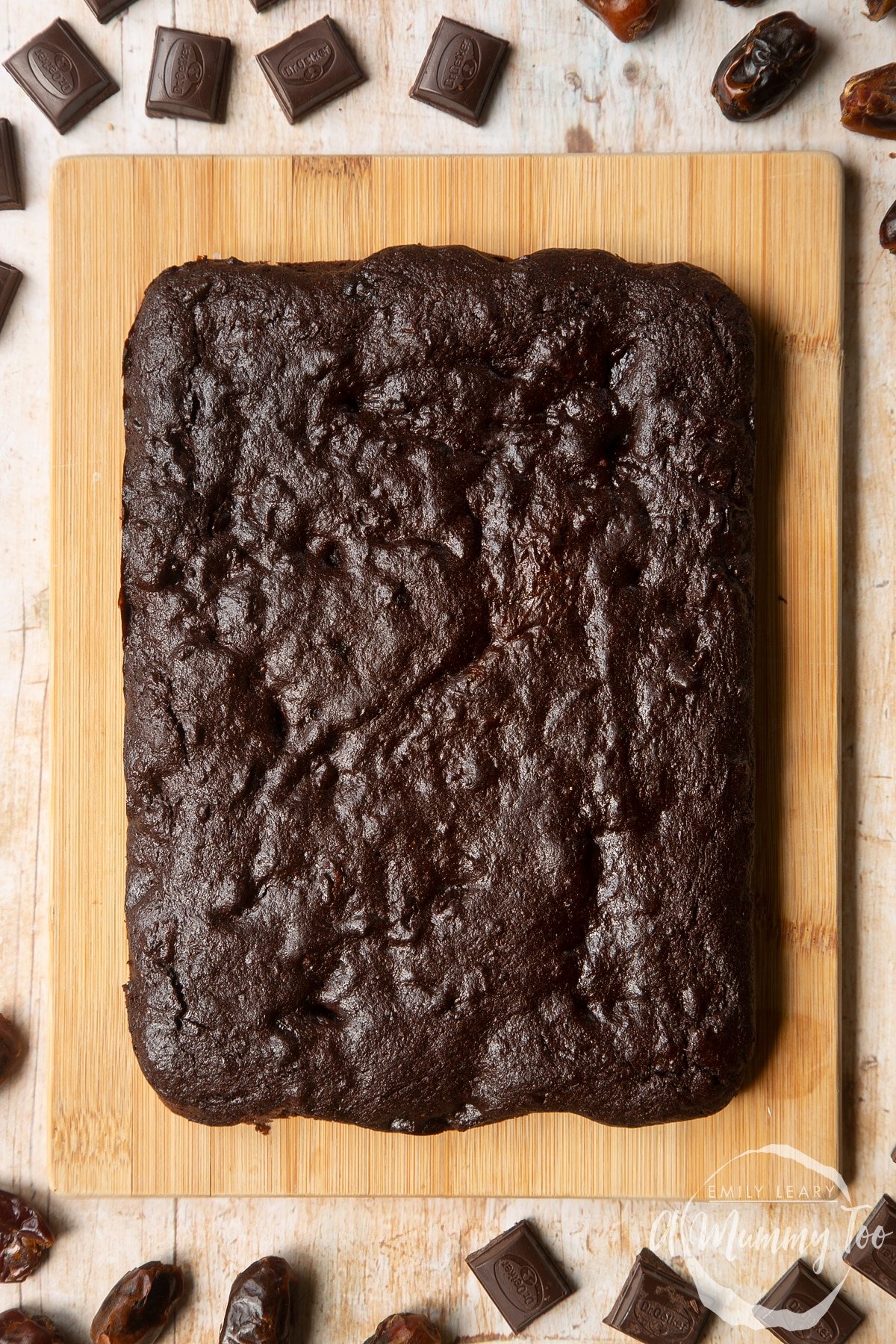 A slab of whole grain brownie on a pale wooden board.