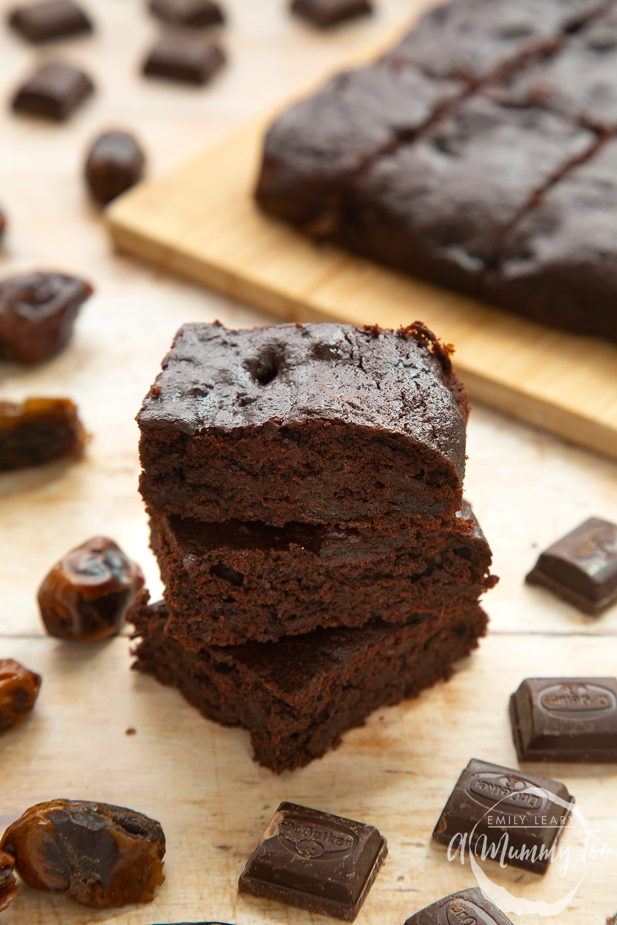Whole grain brownies made with dates and dark chocolate, stacked up on pale wood.