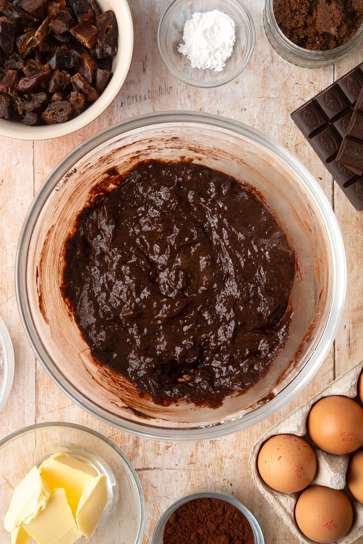 A mixing bowl containing whole grain brownie batter. Ingredients to make whole grain brownies surround the bowl.
